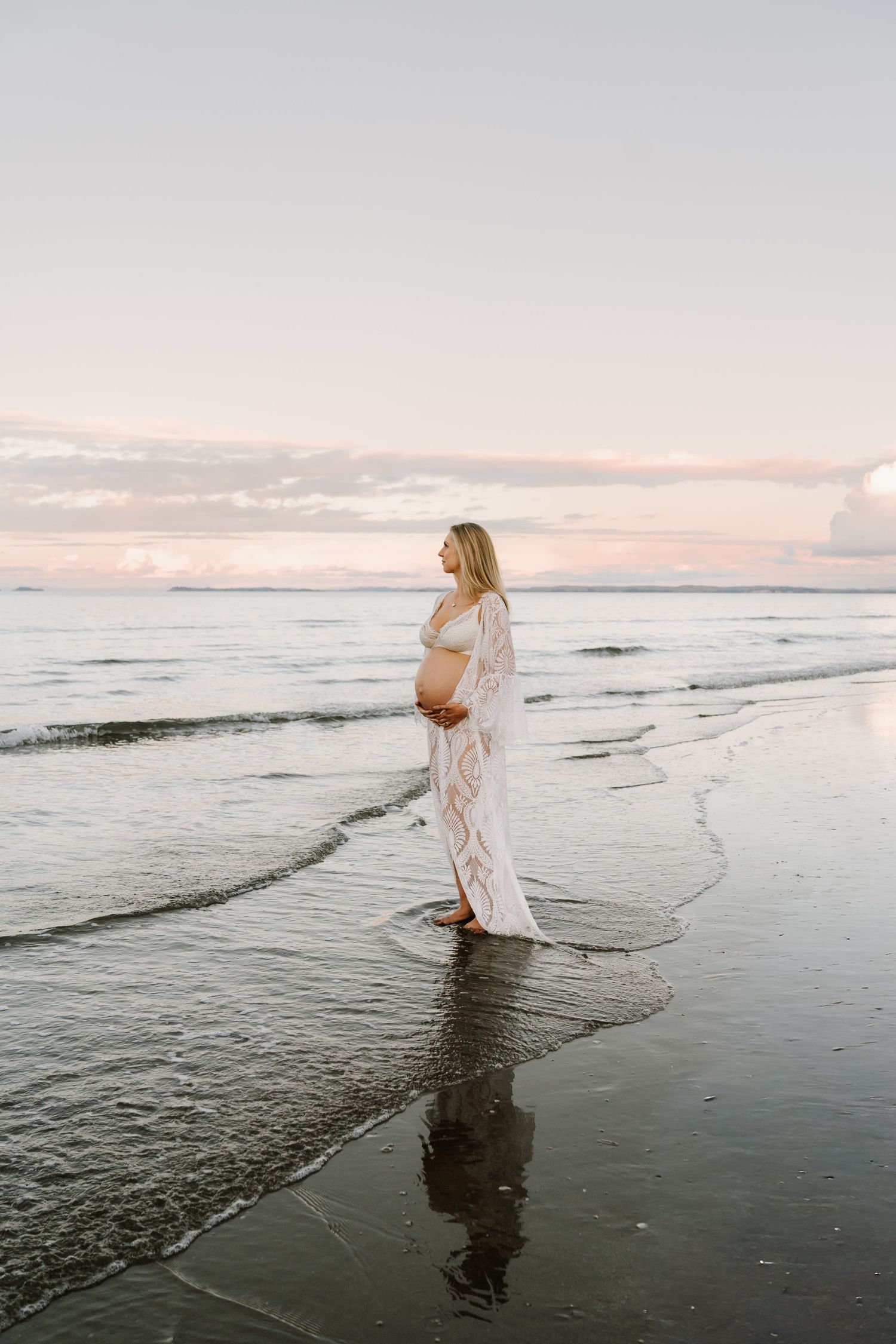 Stunning maternity reflections in the tide at sunset. Bold and modern beach photography by Little Wild Ones, Auckland.