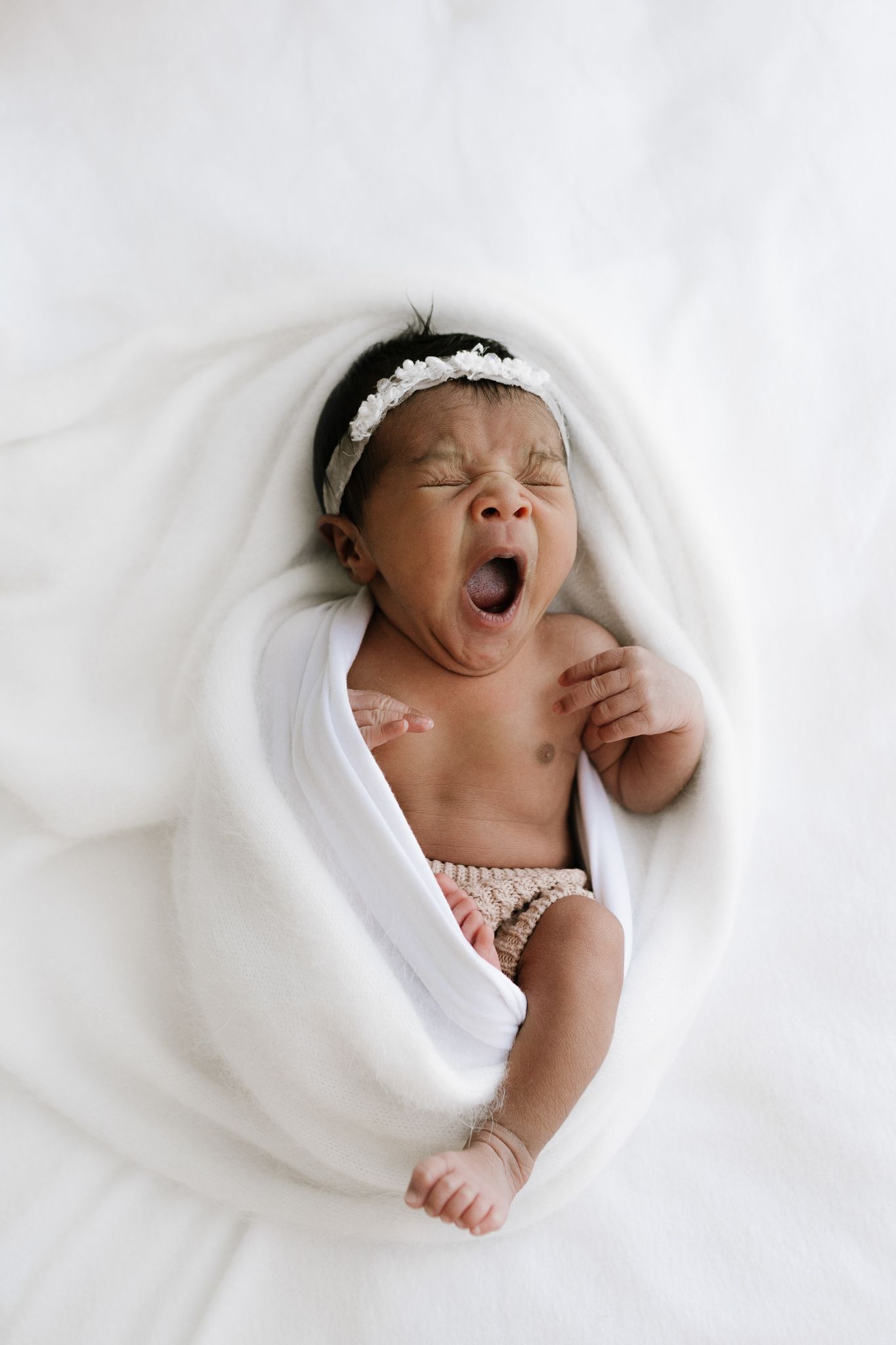 newborn sleeping baby wrapped in white blanket during studio session in Auckland yawning