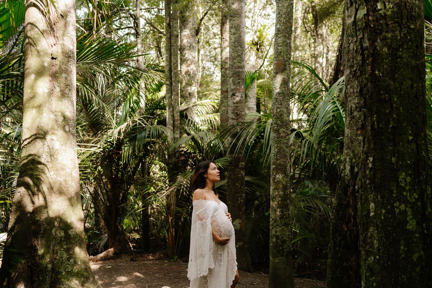 pregnant woman surrounded by native bush, soft light filtering through trees