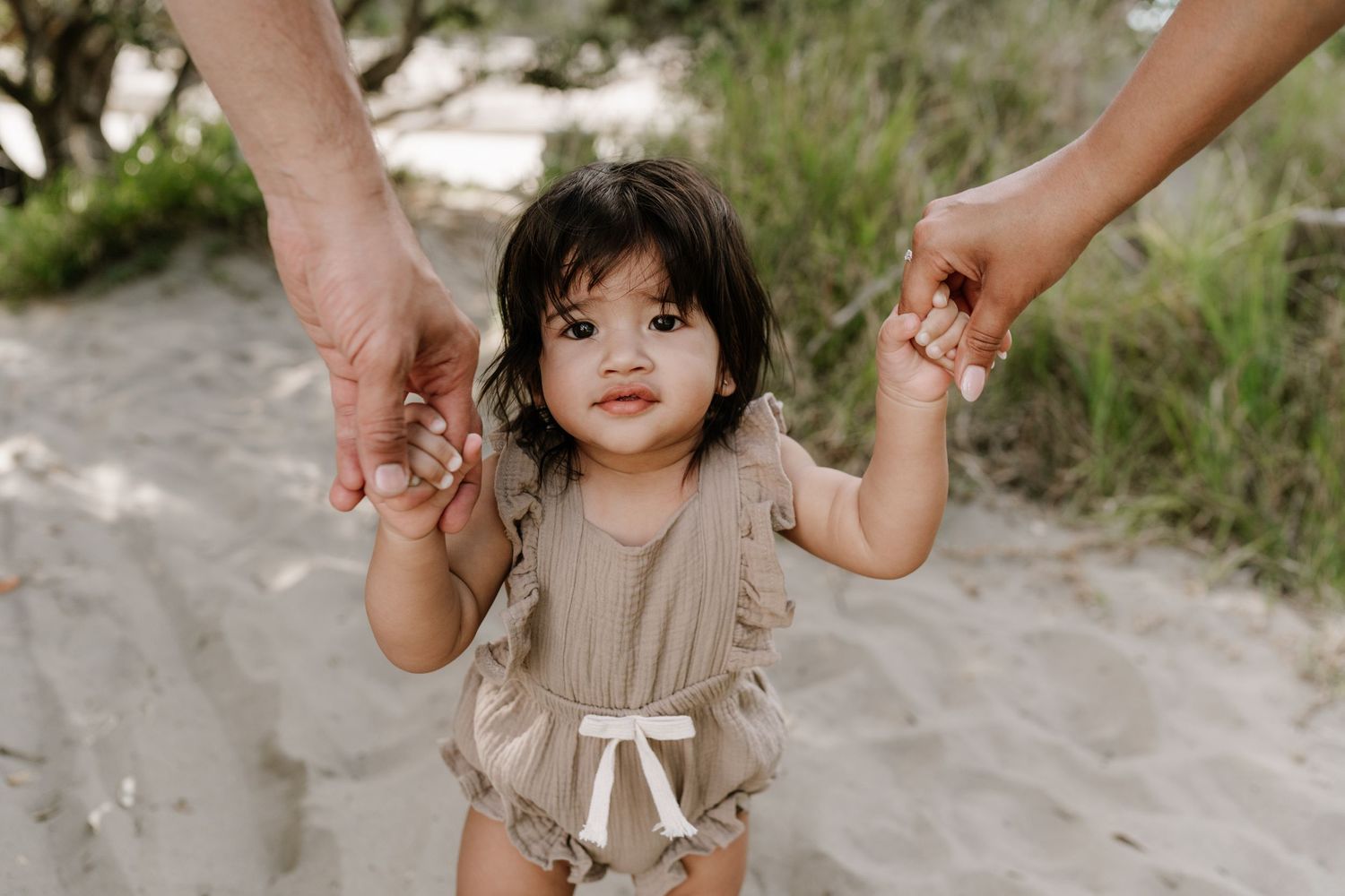 Family photography session with parents holding the hand of child at the beach