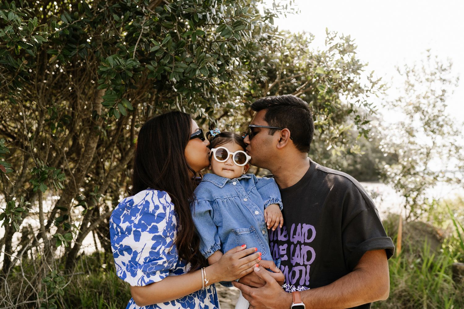 mum and dad kissing baby with sunglasses on at a family session