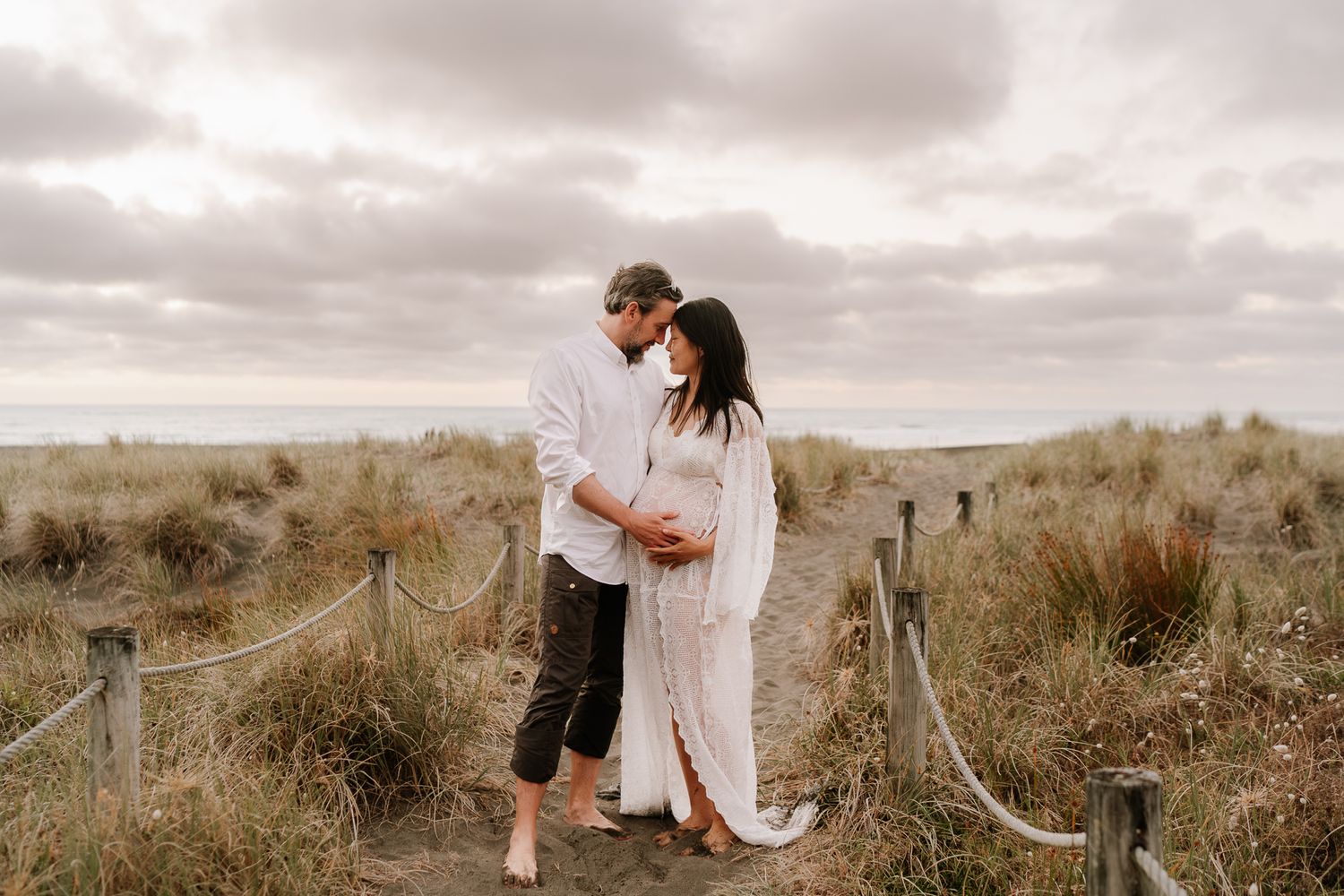 mum and husband holding pregnant belly at beach at sunset