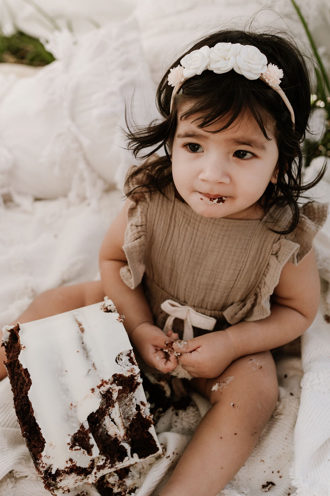 Outdoor cake smash session with a baby seated in front of a teepee, surrounded by long grass. A whimsical, natural setting with playful, mes