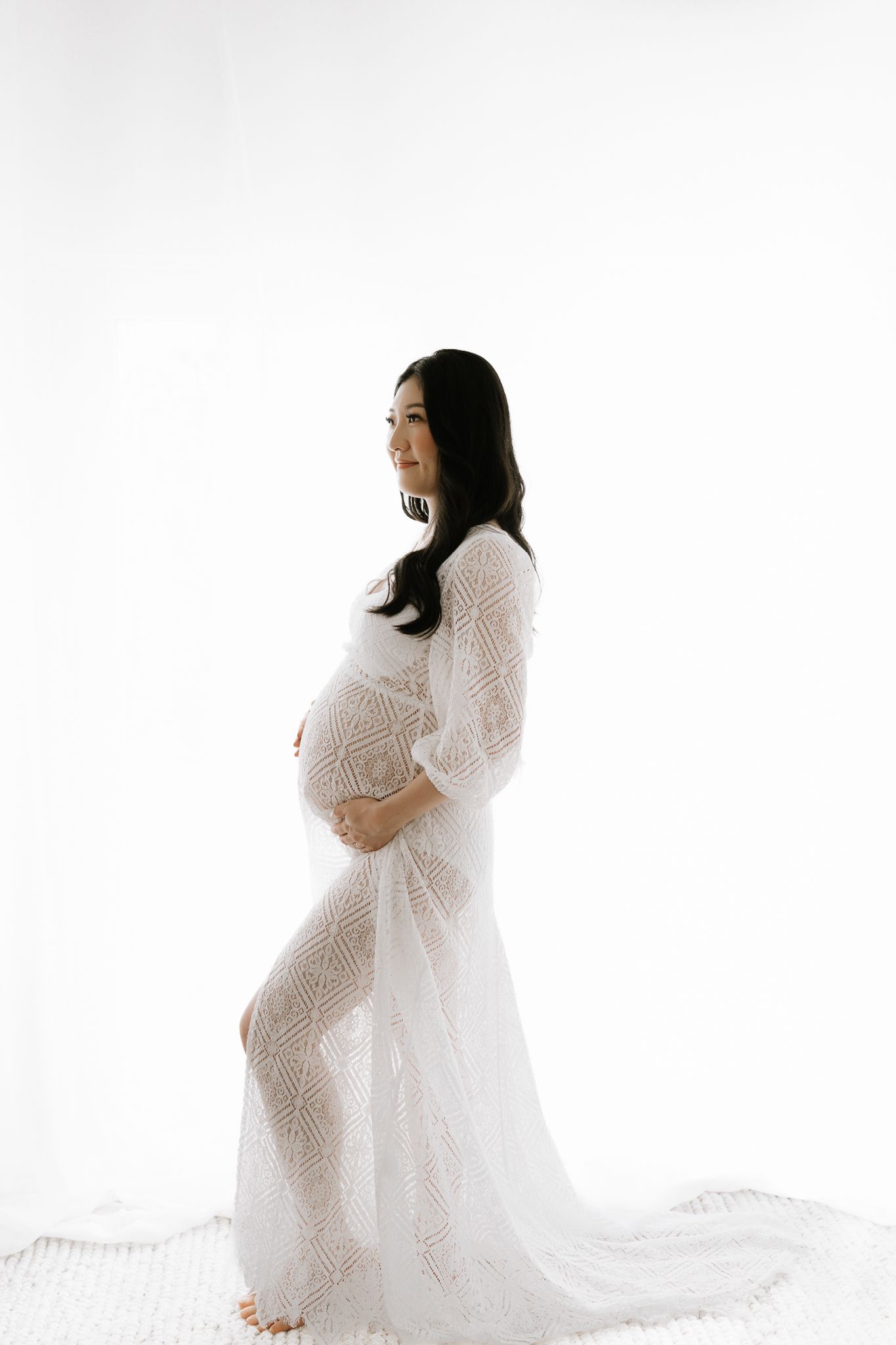 woman in white studio dress showing pregnant belly