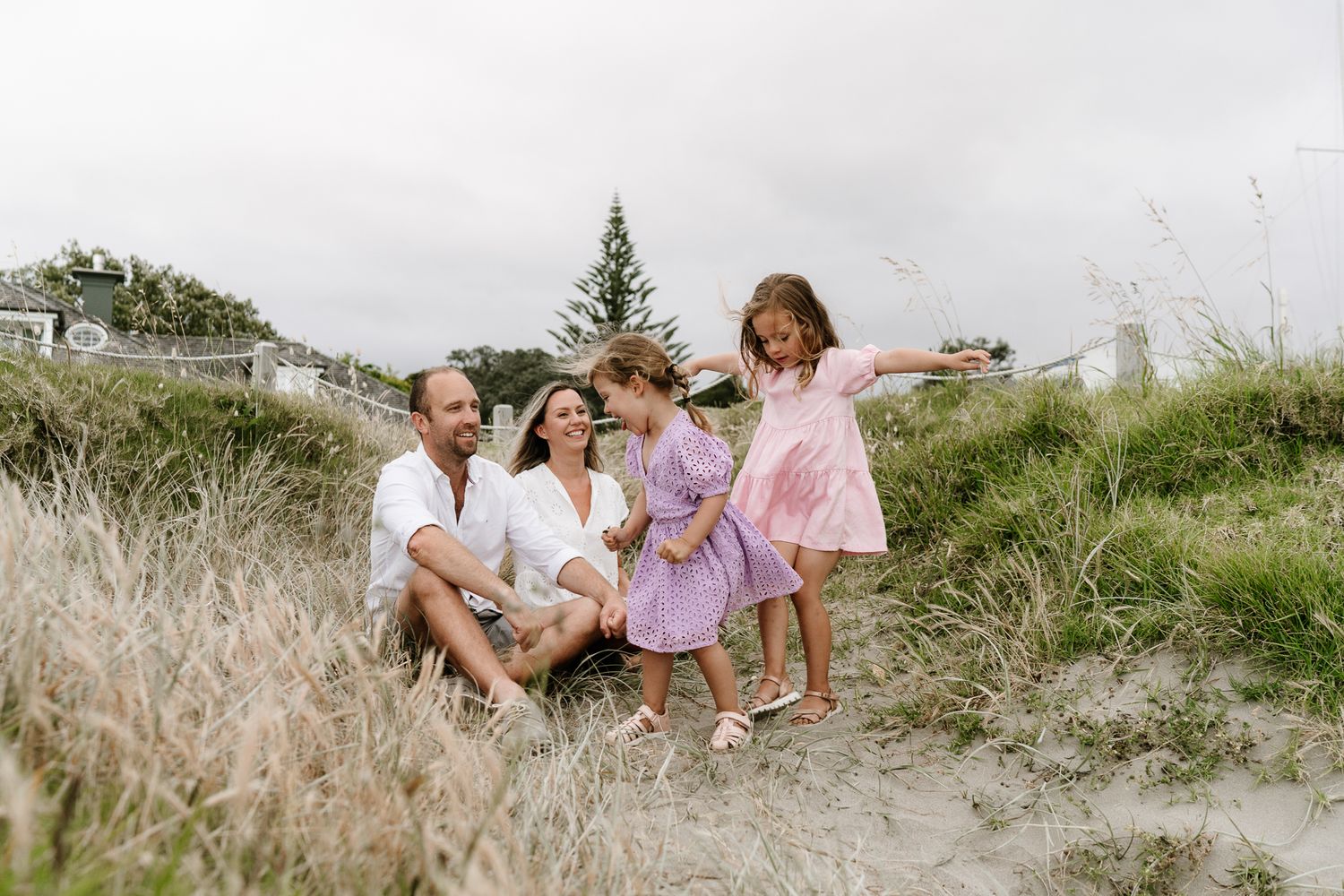 Family photography session with parents and two young children playing and cuddling outdoors. Natural light, joyful expressions, and candid