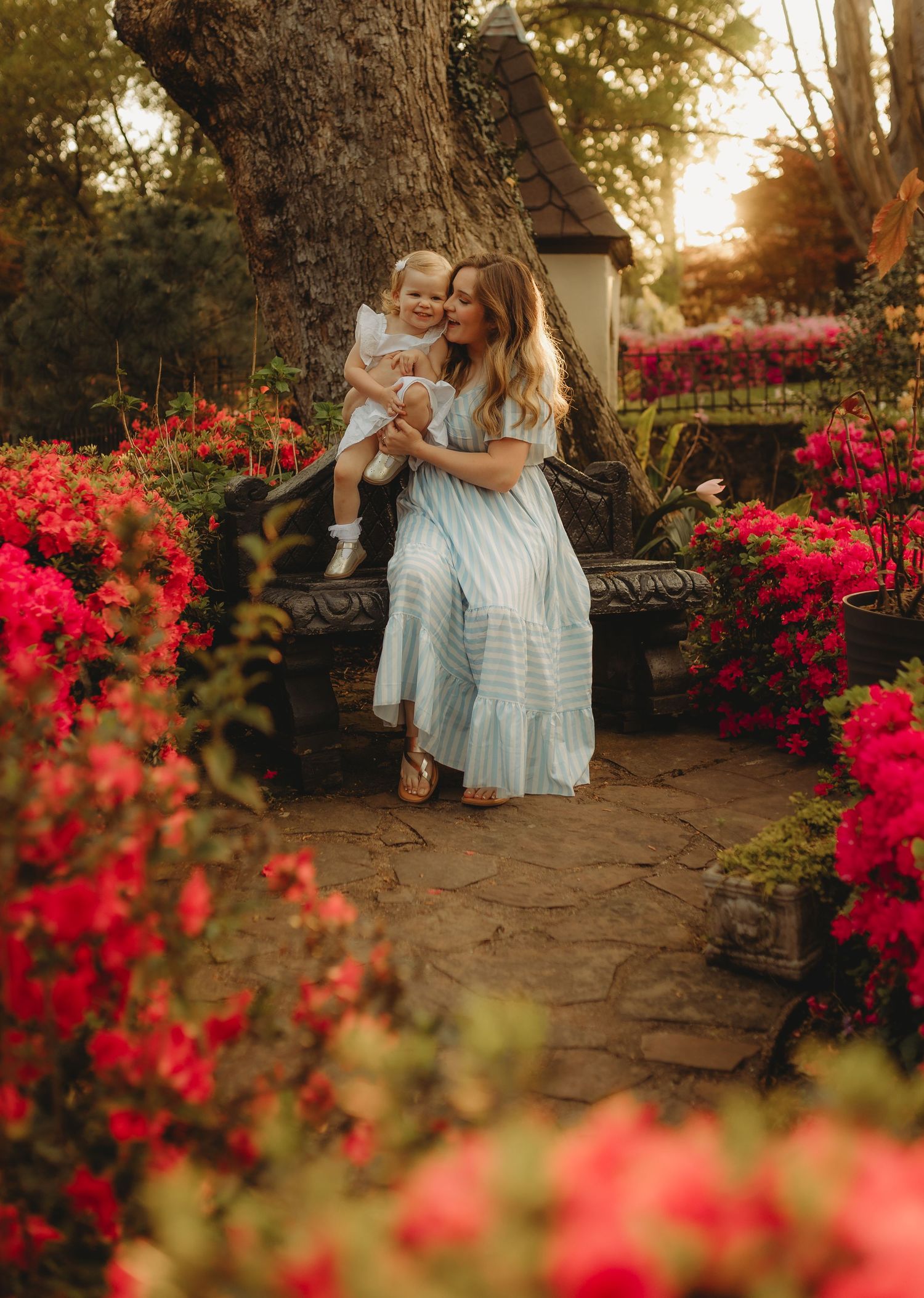 A romantic sunset photoshoot in a garden with vibrant red flowers and stone pathway creating a dreamy atmosphere.