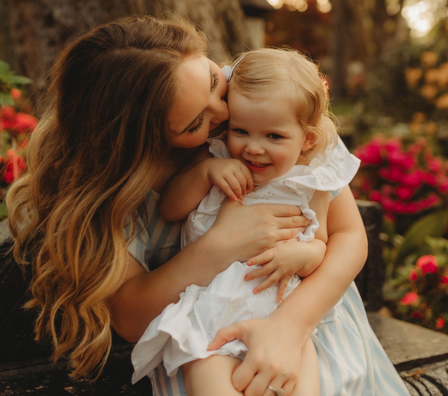 A tender moment between parent and child in a garden setting with warm lighting and blooming flowers in the background.