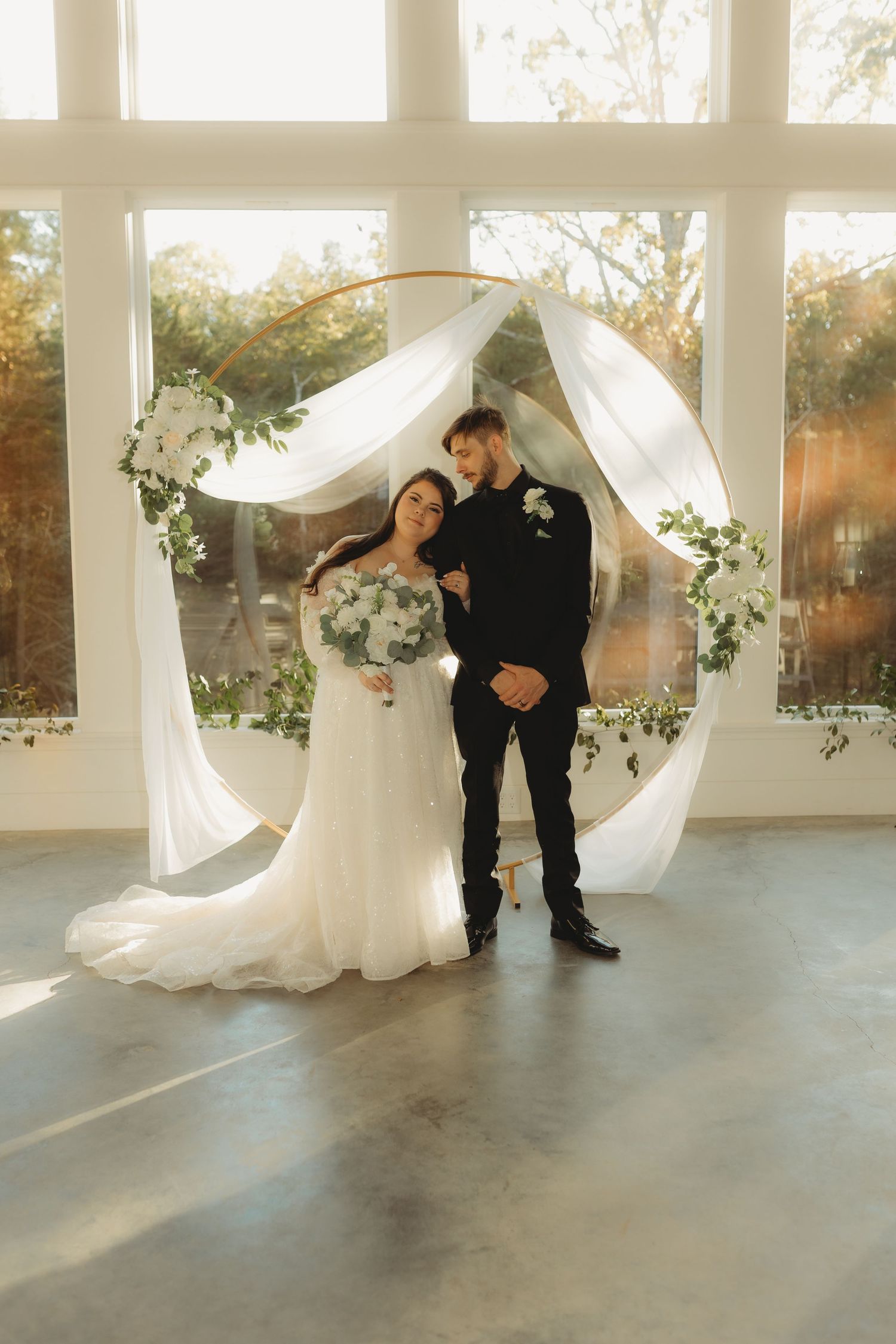 A romantic wedding couple shares an intimate moment in a sun-filled room with white draping and pillars.