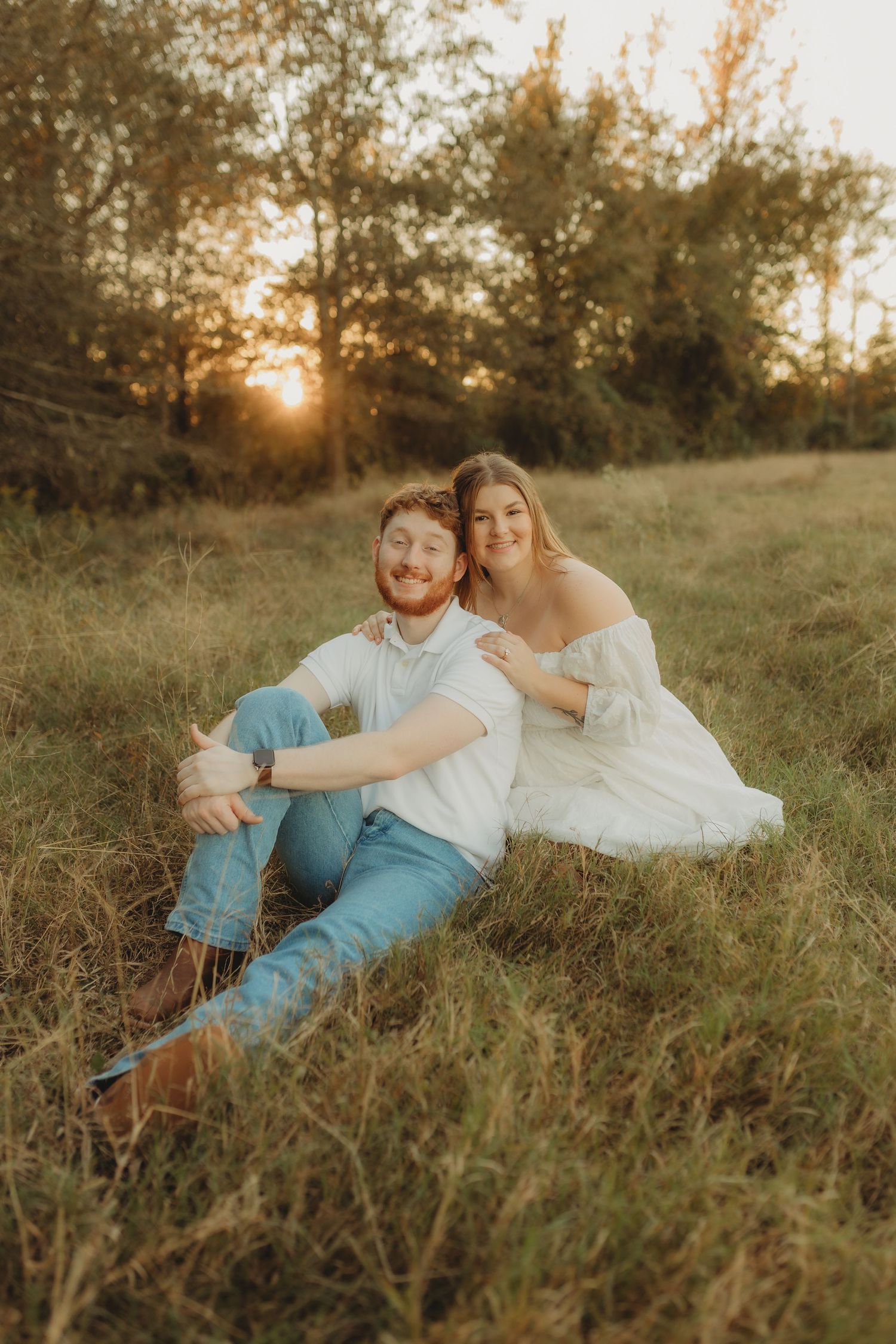 Couple lying together in golden sunlit meadow during romantic sunset photo session.