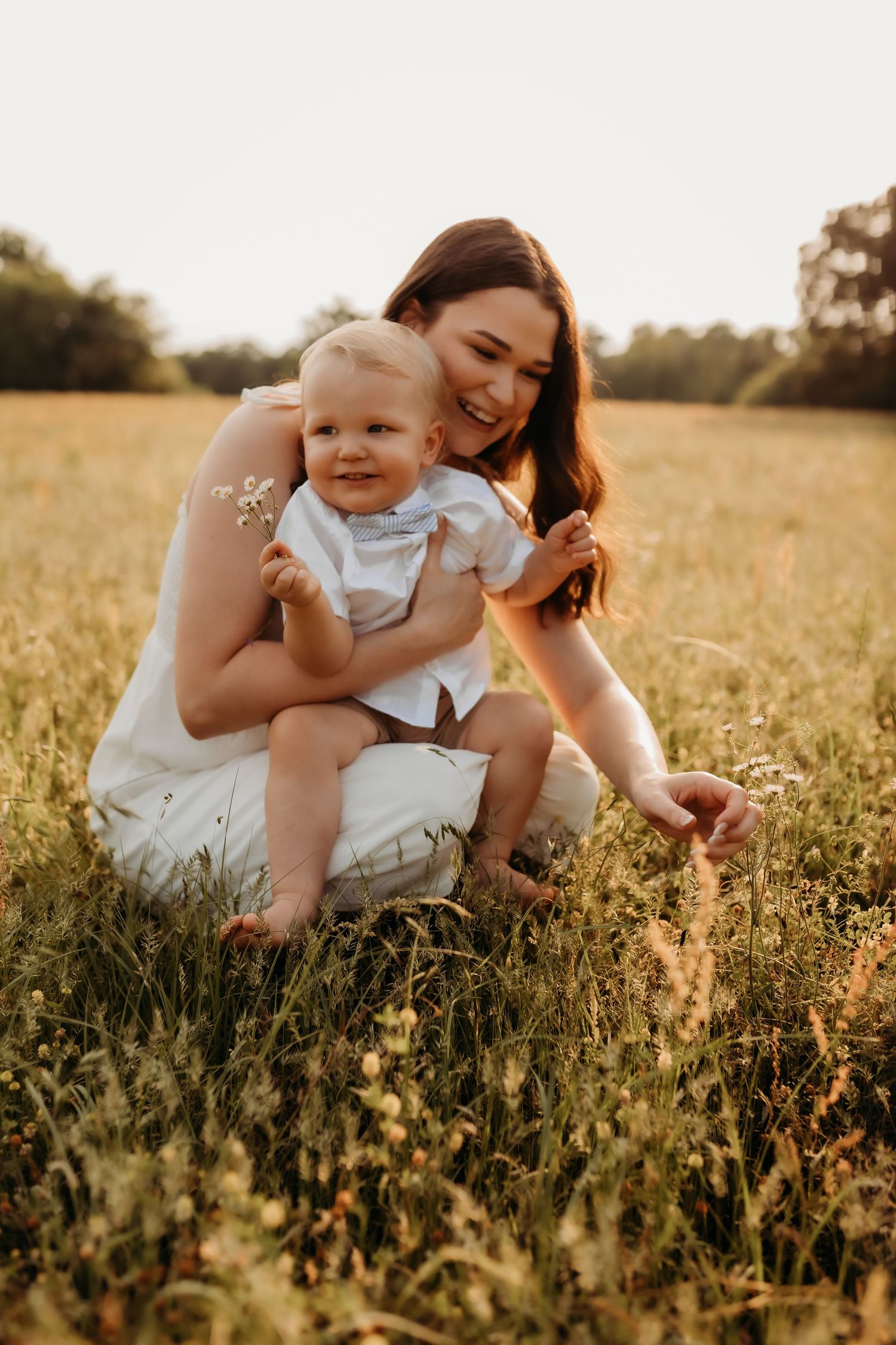 A parent and baby share tender moments while sitting in a wildflower field at golden hour.