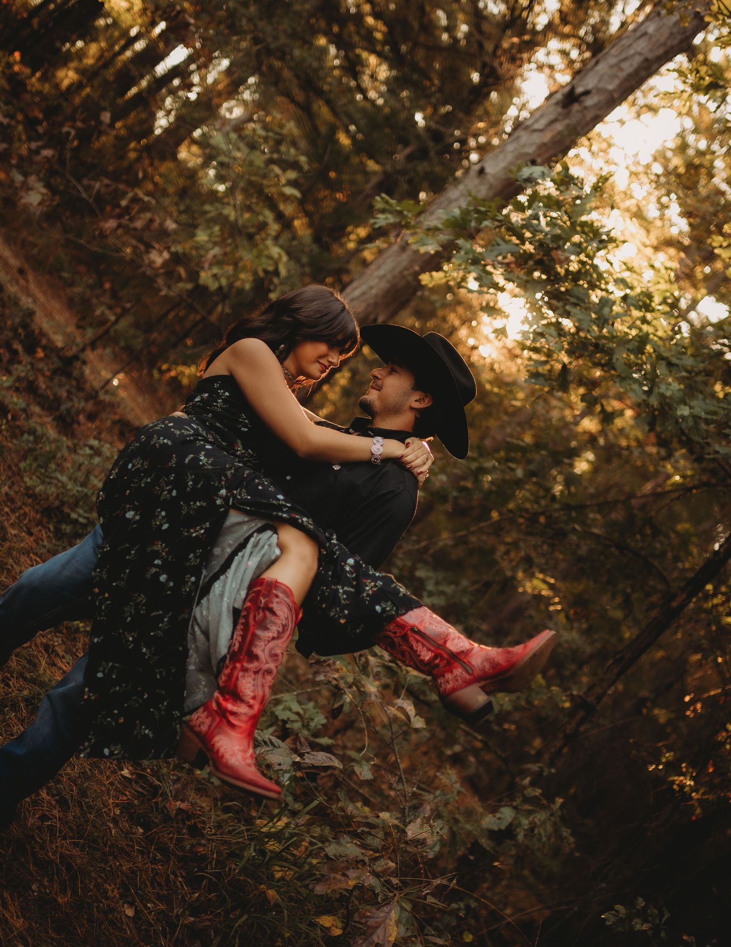 Two figures share an intimate embrace while perched on a tree branch at sunset in a dreamy autumn forest setting.