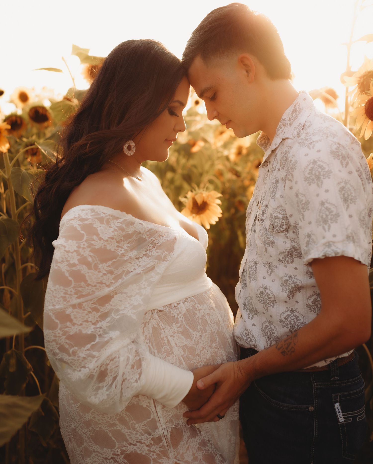 A romantic couple embraces in a sunlit field of sunflowers during golden hour.