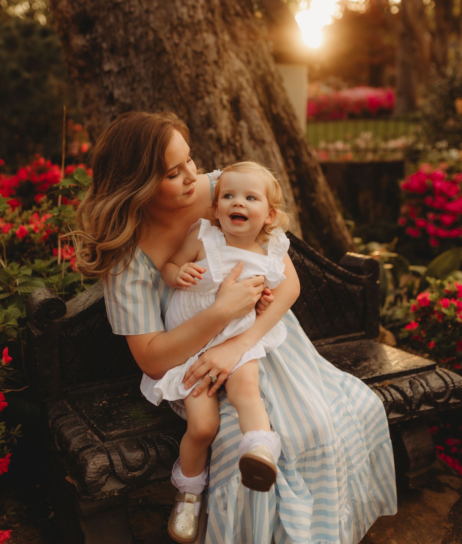 A tender moment captured in a garden with blooming red flowers during golden hour sunset lighting.