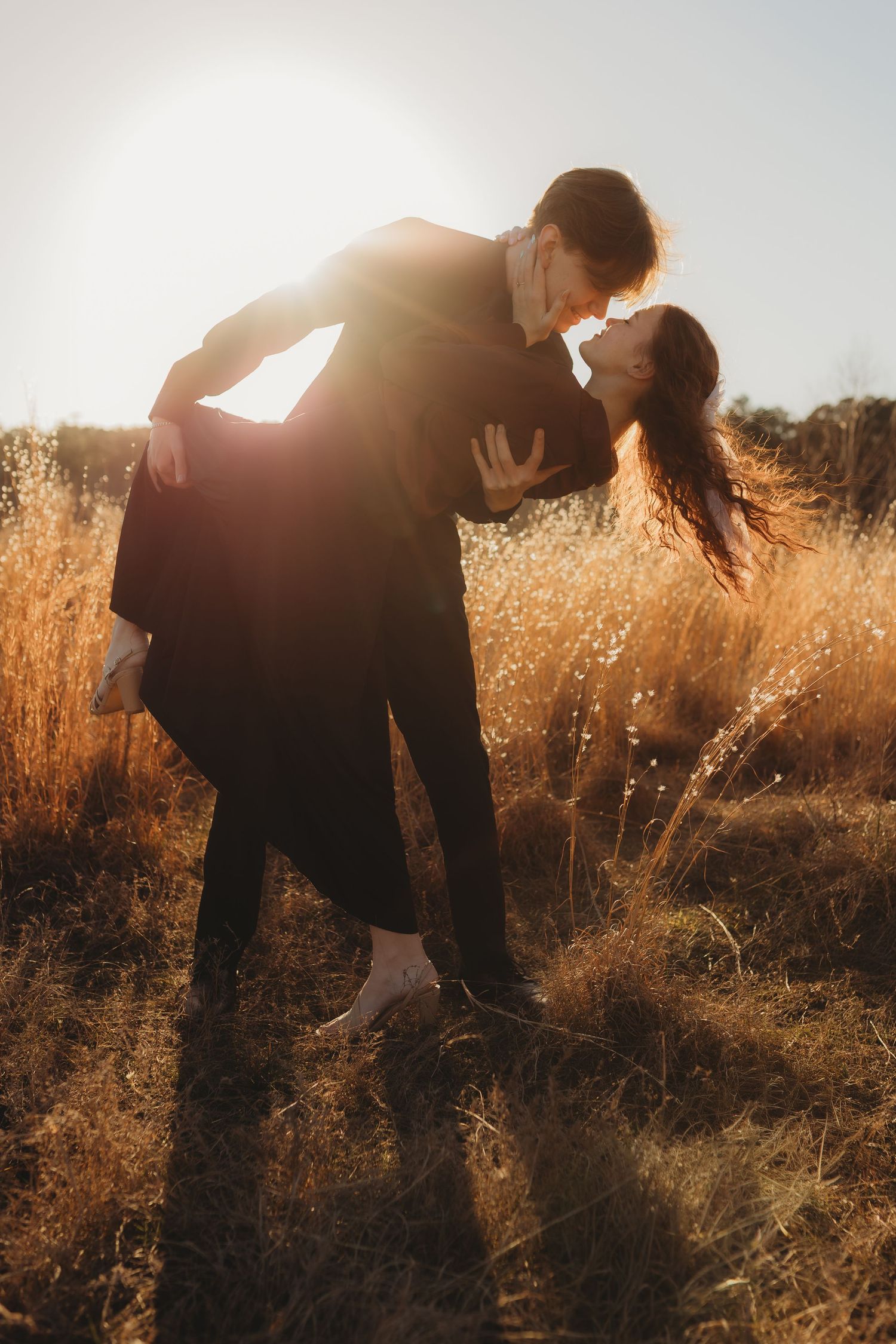 Silhouetted couple sharing romantic moments in golden sunlit field during sunset.