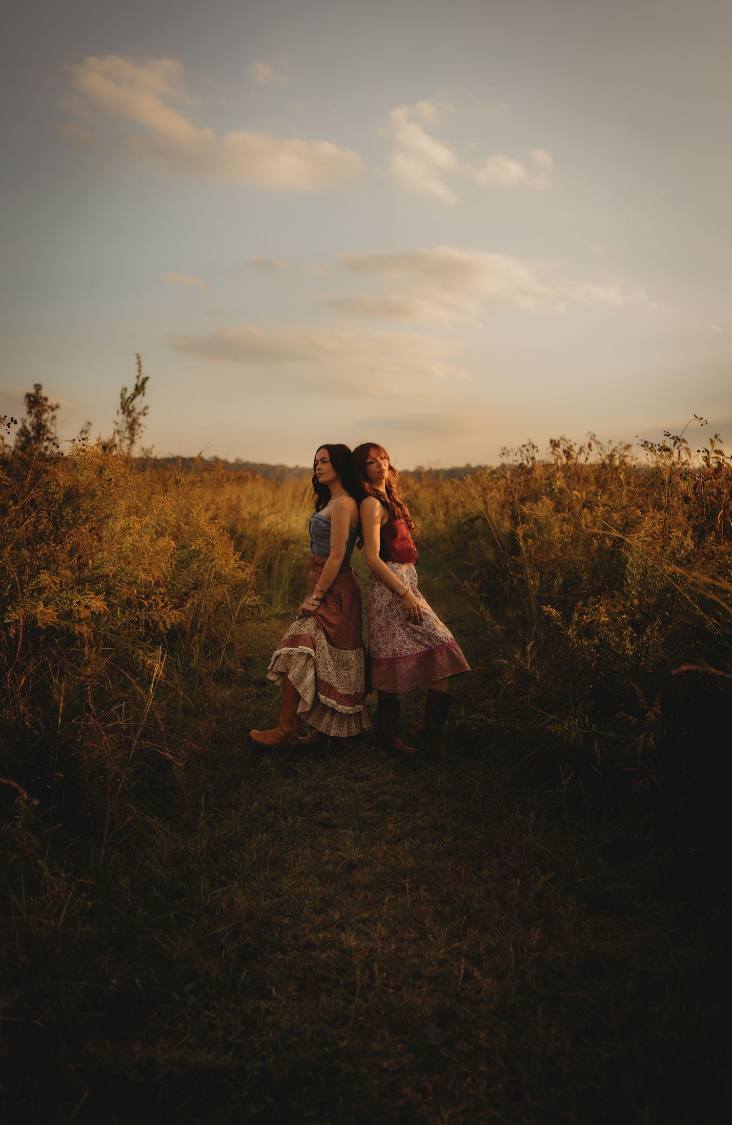 Two figures in flowing dresses dance together in a golden field at sunset, creating a dreamy silhouette against the sky.