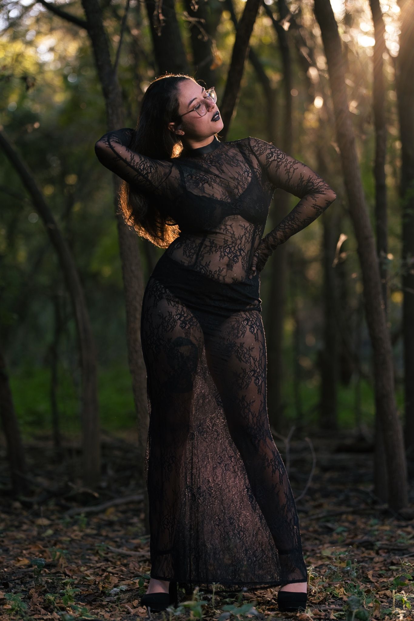 A person in a black lace dress dances gracefully through a sunlit forest during golden hour.