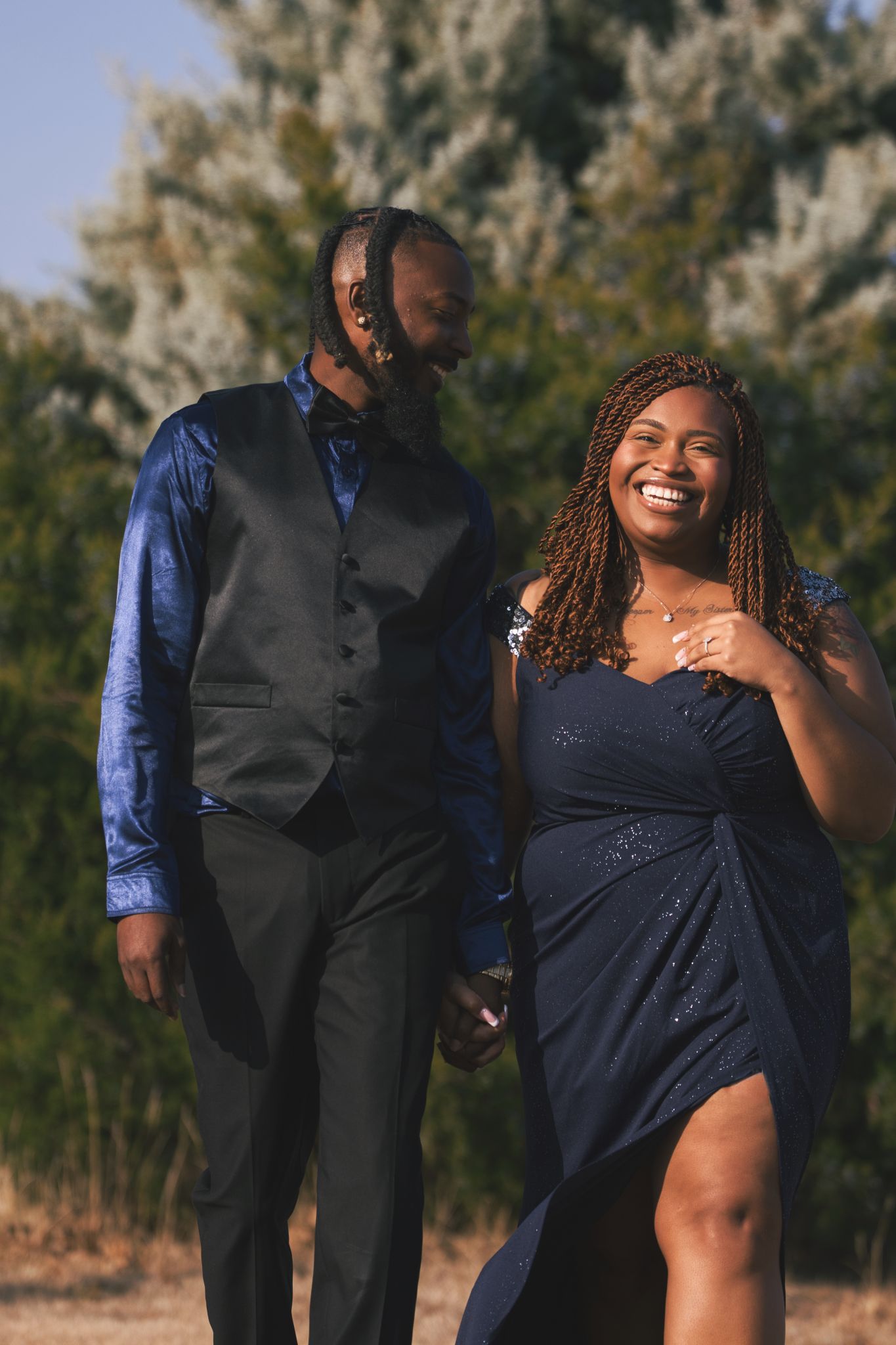 A couple in formal navy blue attire shares a joyful moment together during an outdoor photoshoot.