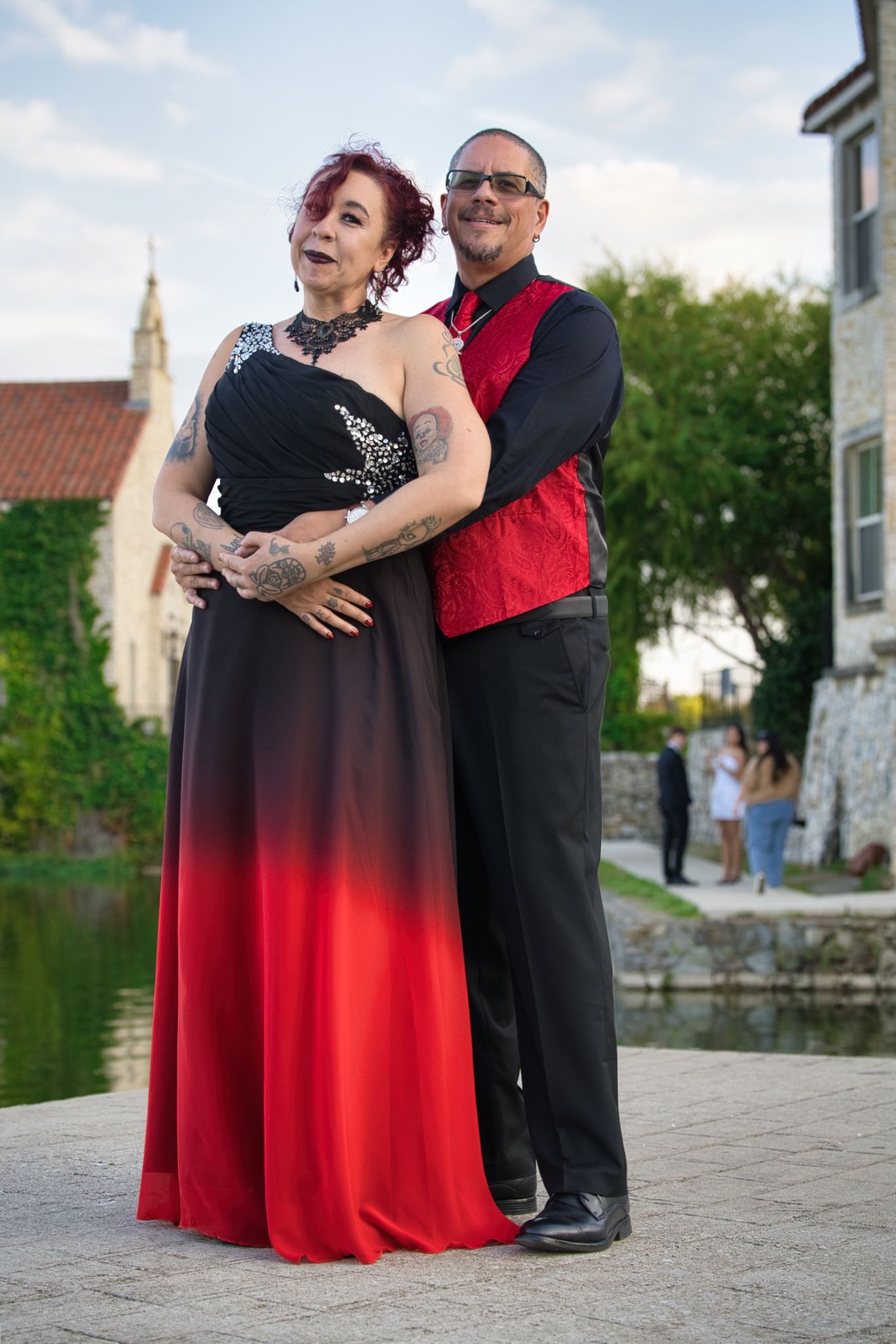 Couple in elegant attire shares romantic moment by waterfront during sunset.
