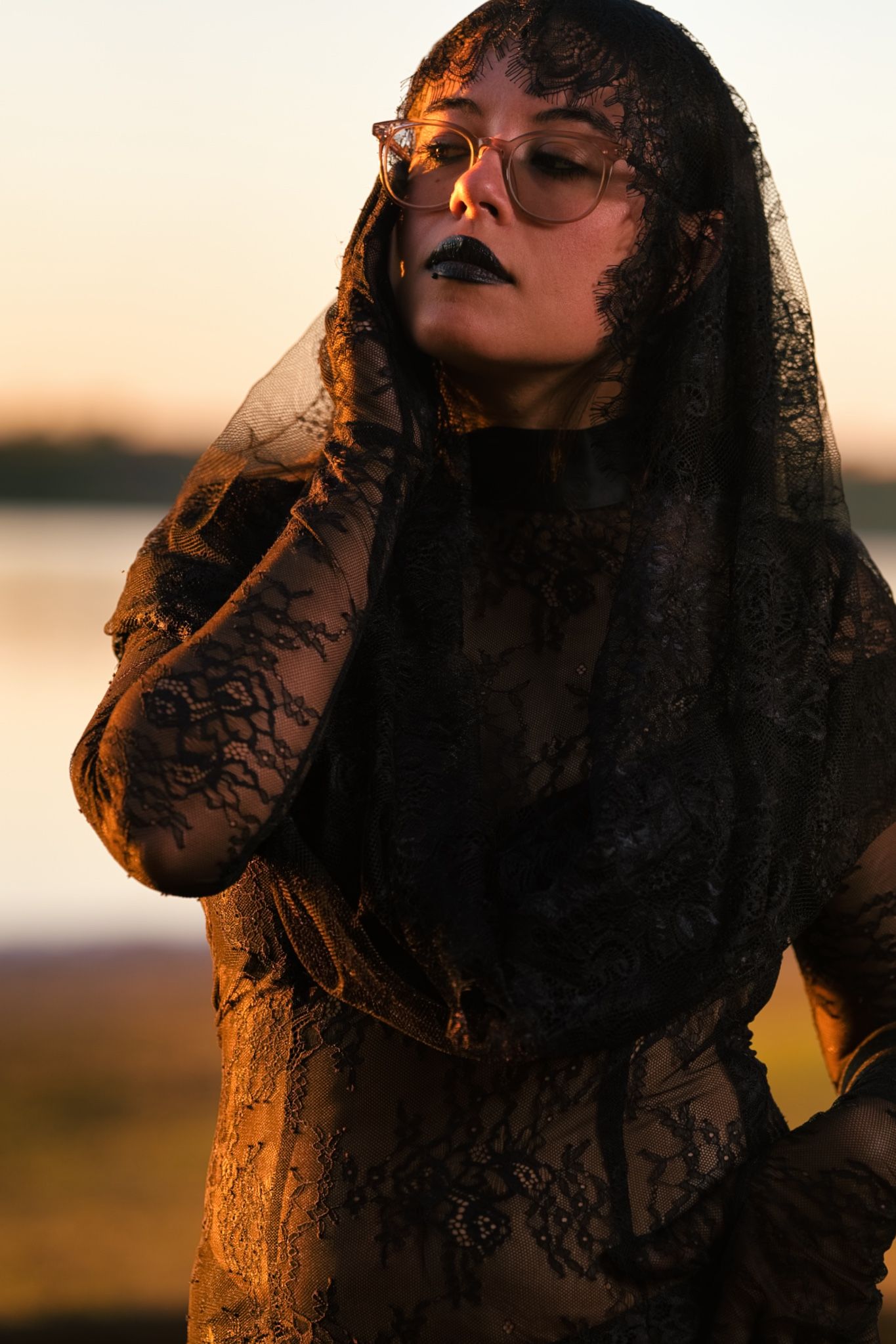 A gothic fashion portrait in black lace veil during golden hour sunset.