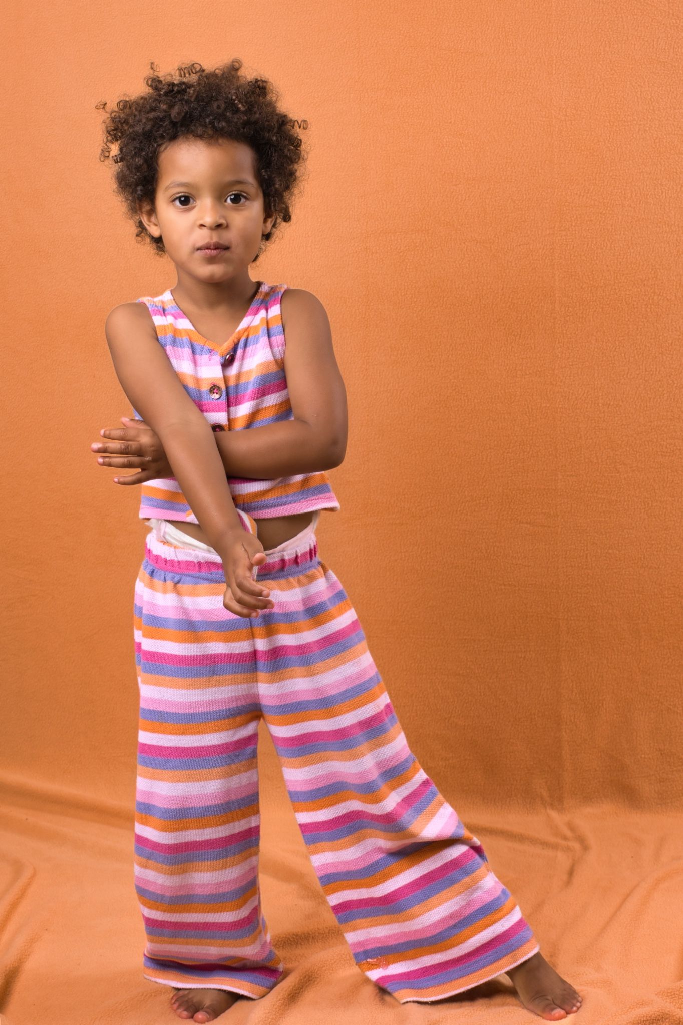 A child in a colorful striped jumpsuit poses playfully against an orange backdrop in a series of candid shots.