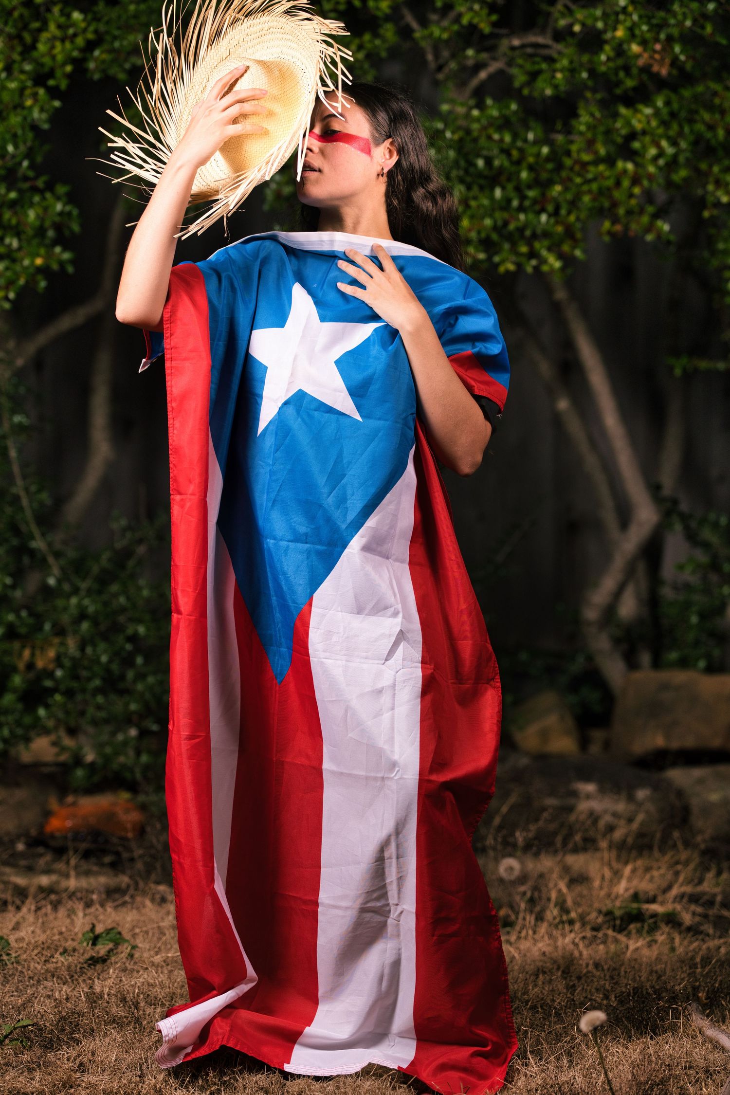 A person wearing a Chilean flag as a cape poses dramatically outdoors against a green foliage background.
