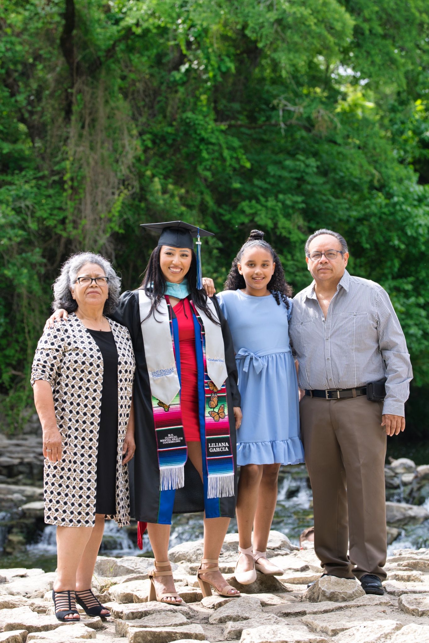 Family poses together on rocky outcrop near waterfall during graduation celebration.