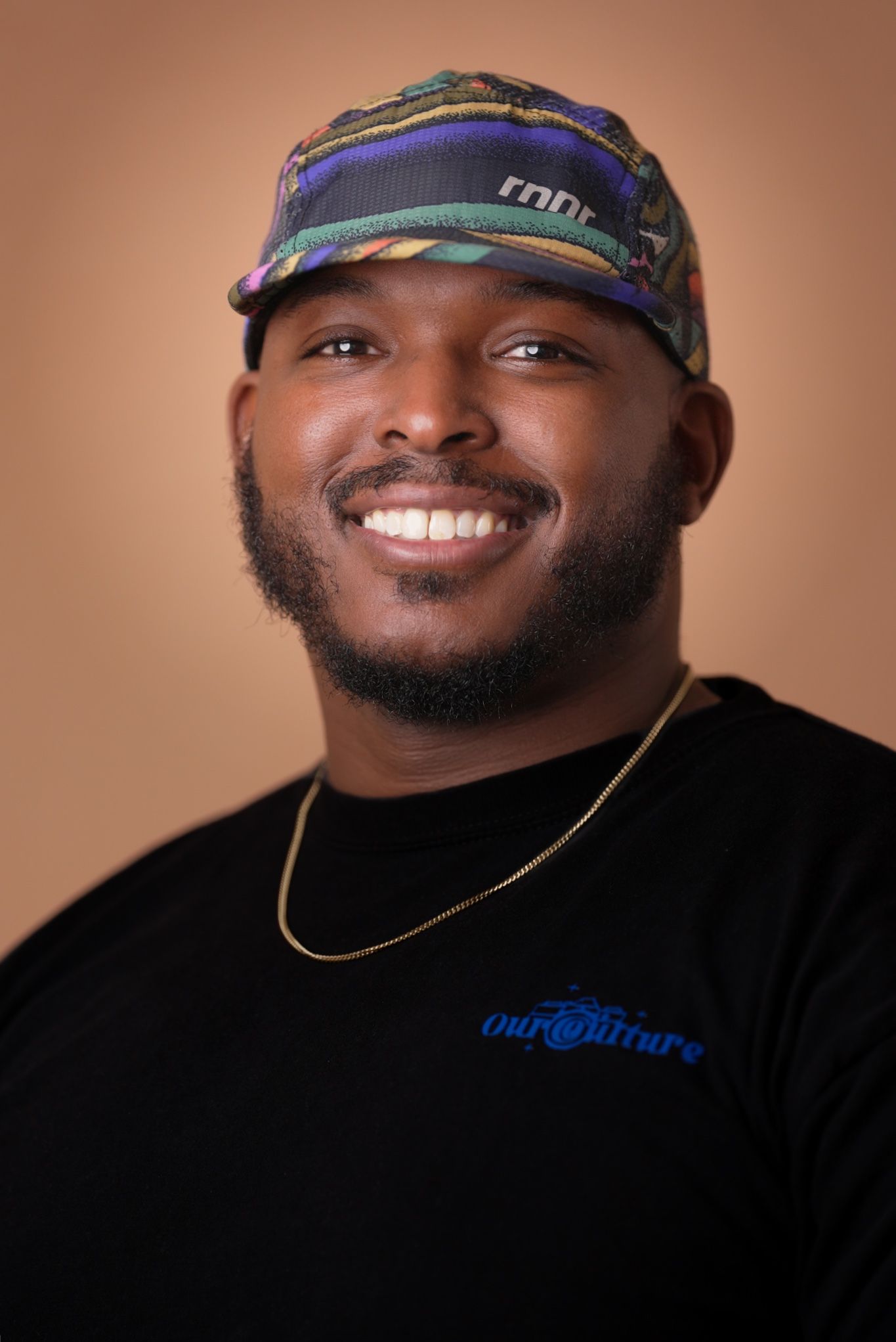 Portrait of person wearing colorful cap and black shirt against warm background.