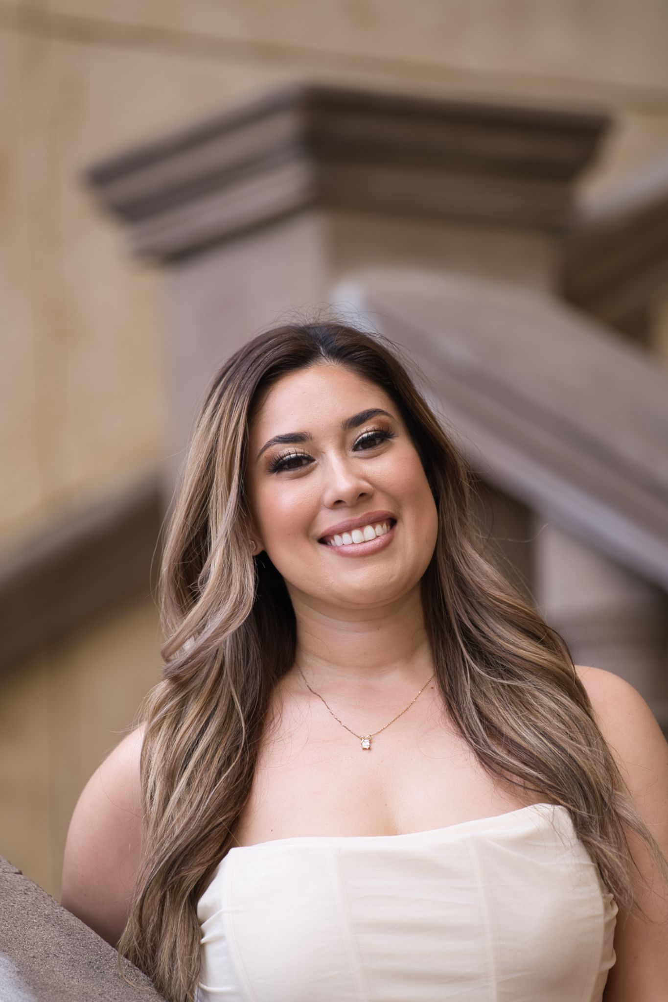 Professional headshot of someone in a white dress smiling against architectural background.