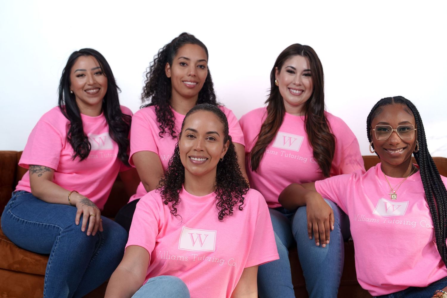 Group of women wearing matching bright pink t-shirts smile together in a casual photo shoot setting.
