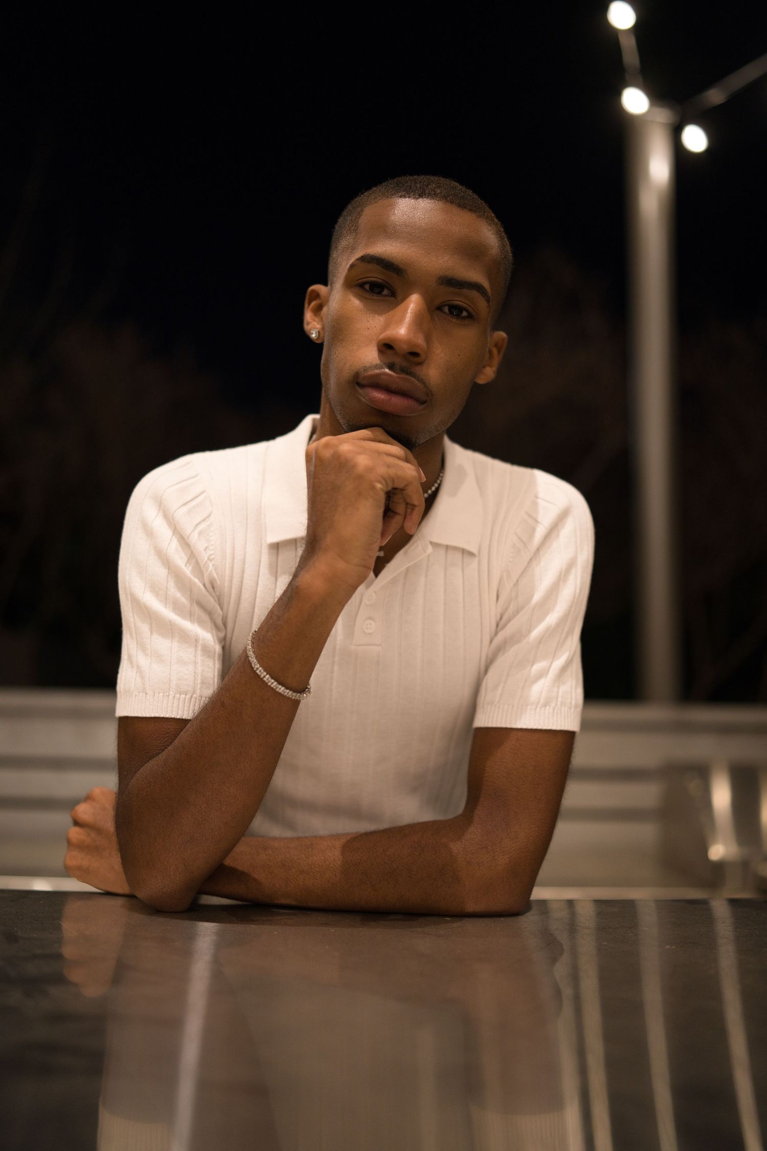 Portrait of someone in a white polo shirt sitting at a table with string lights in the background.