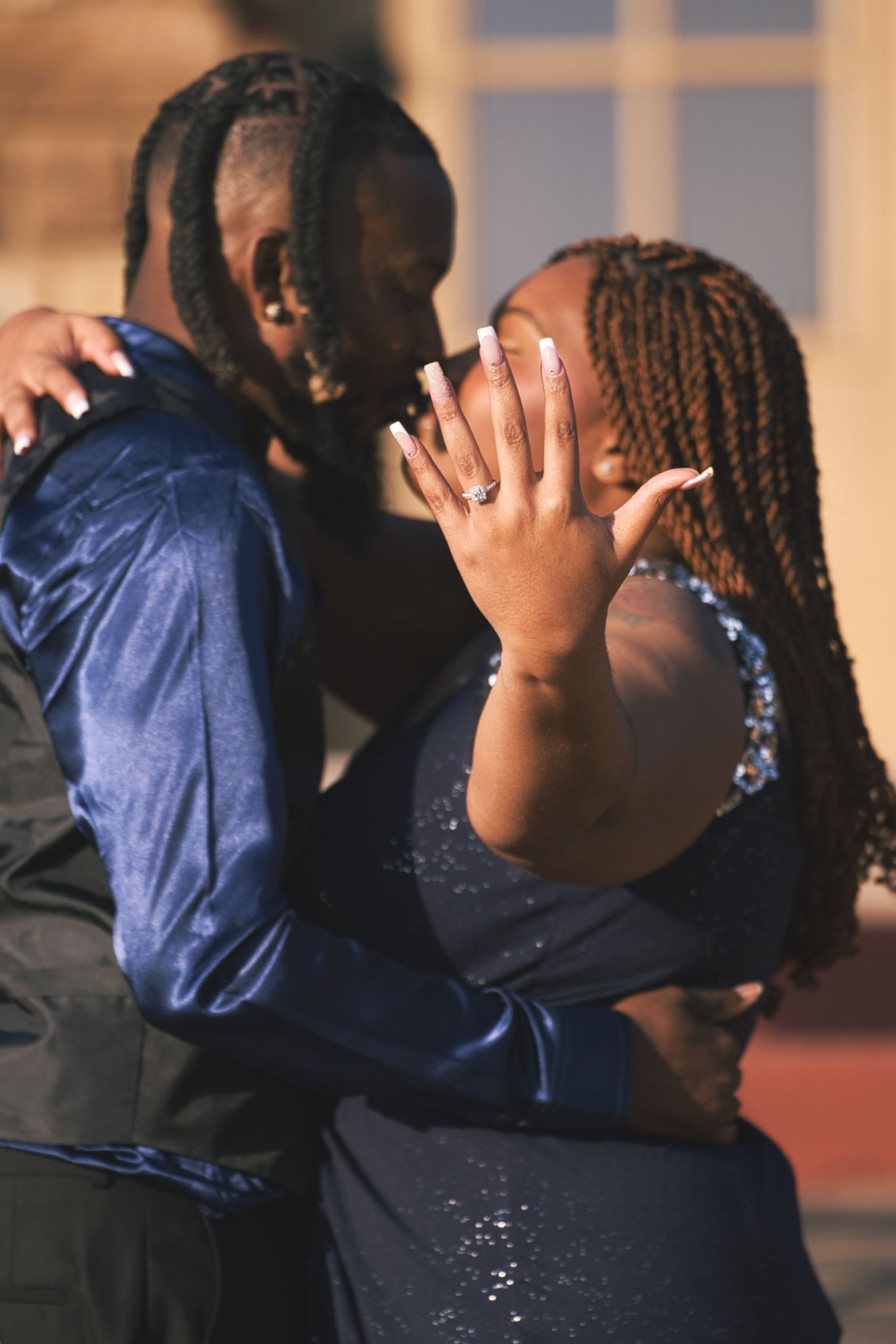 Two people share an intimate moment together, one covering their face while wearing a navy blue outfit.