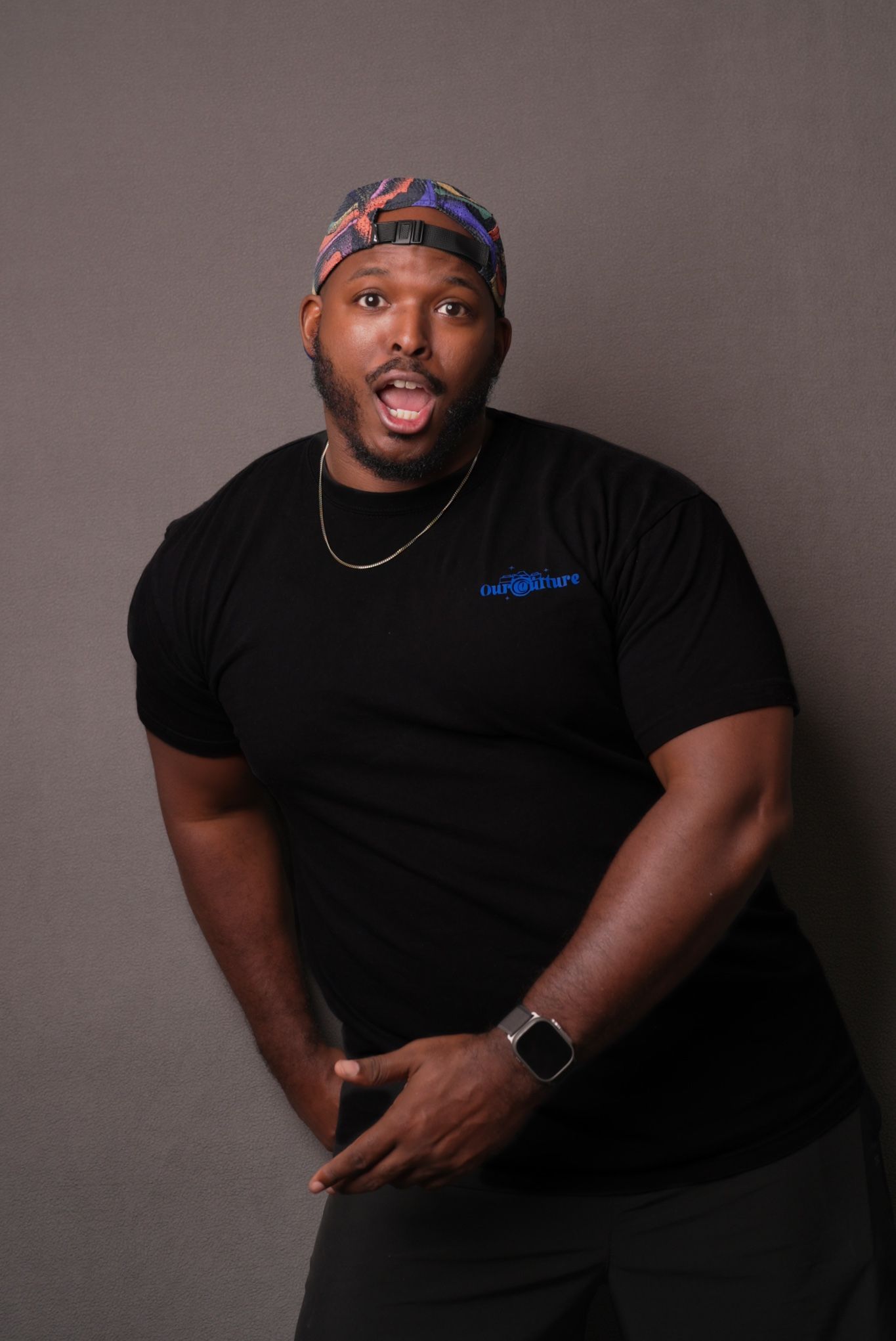 Person wearing a colorful headband and black t-shirt poses against grey studio background.
