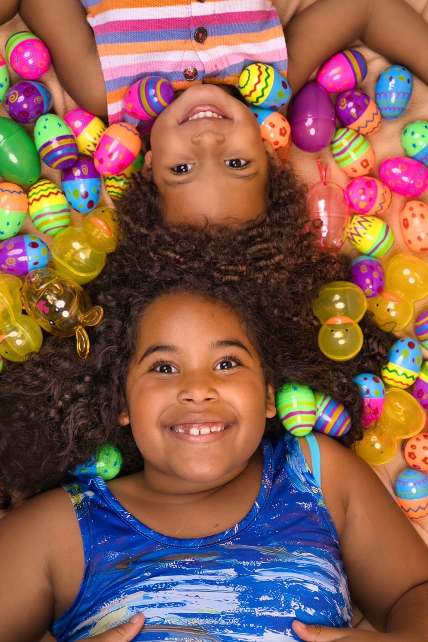 Colorful plastic Easter eggs surround someone wearing blue while lying down and smiling at the camera.