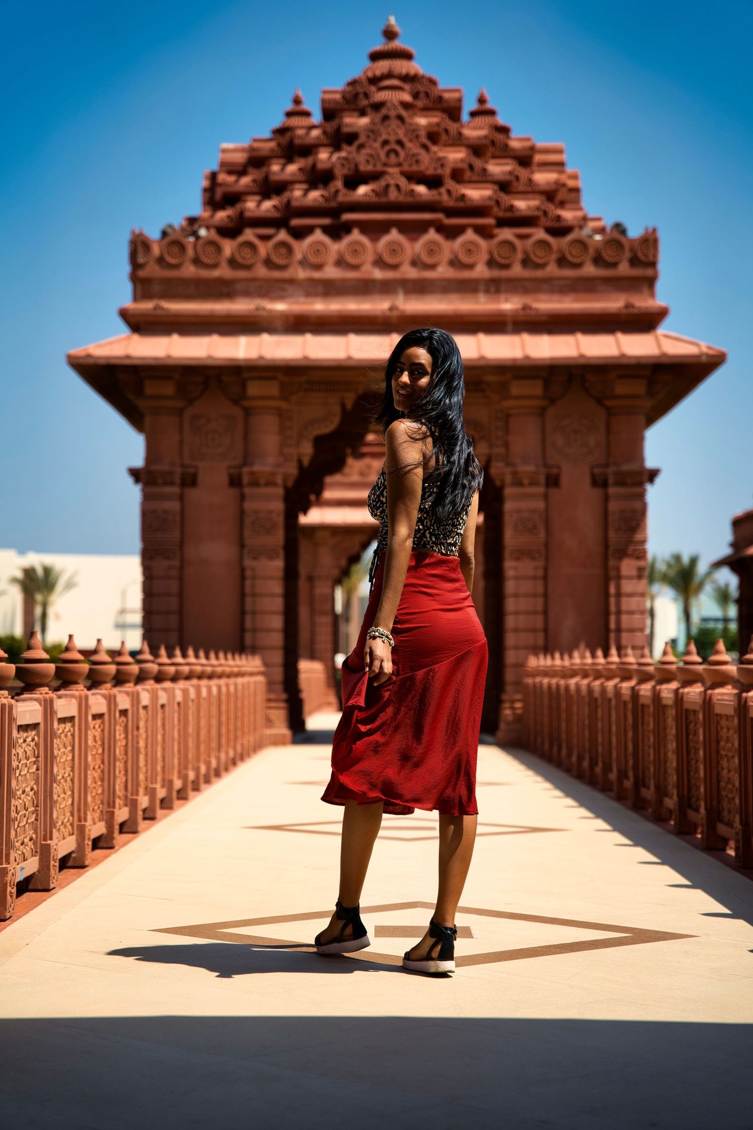 Red dress silhouette against ornate temple architecture in warm sunlight.
