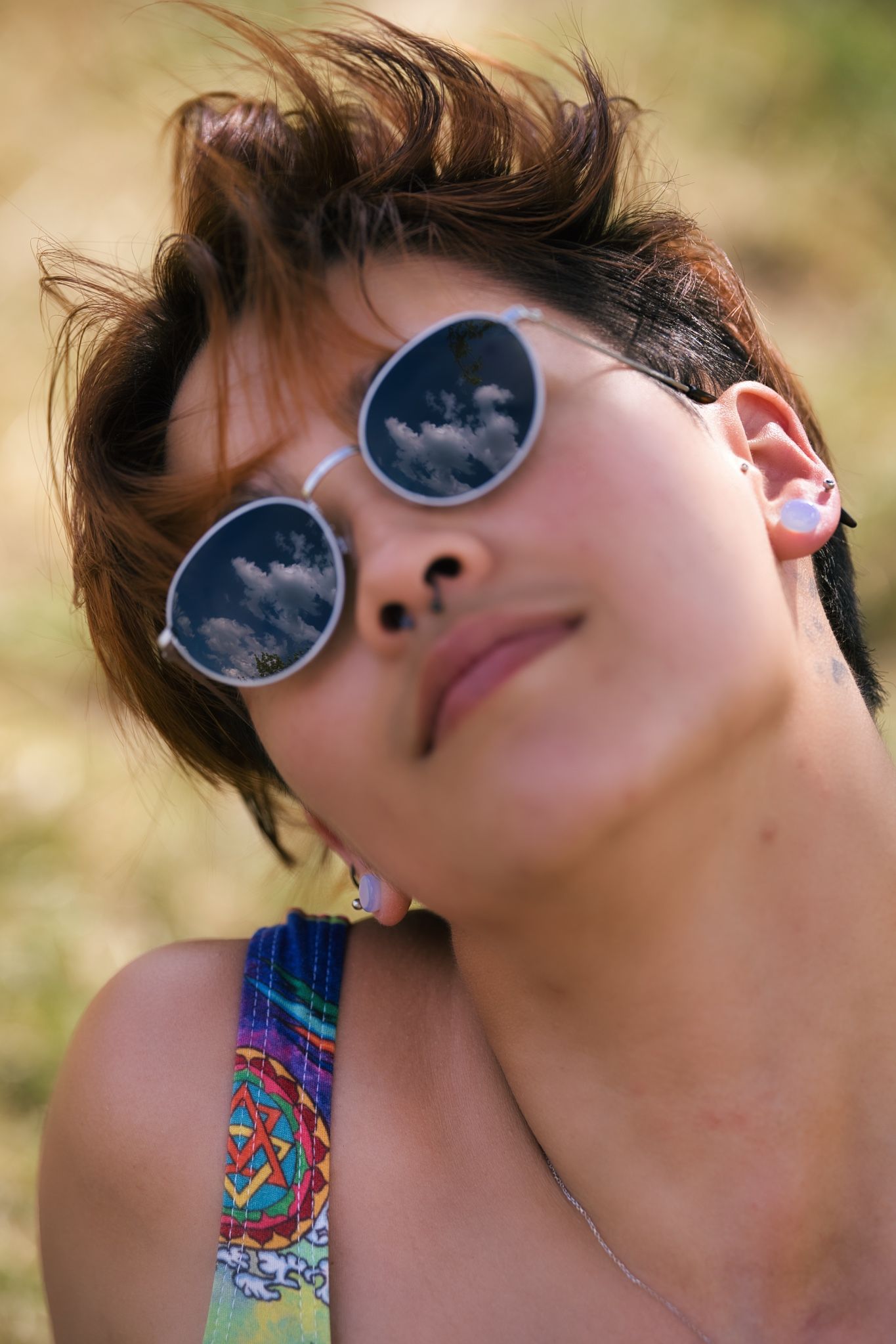 Round sunglasses reflect clouds while worn in artistic summer portrait.
