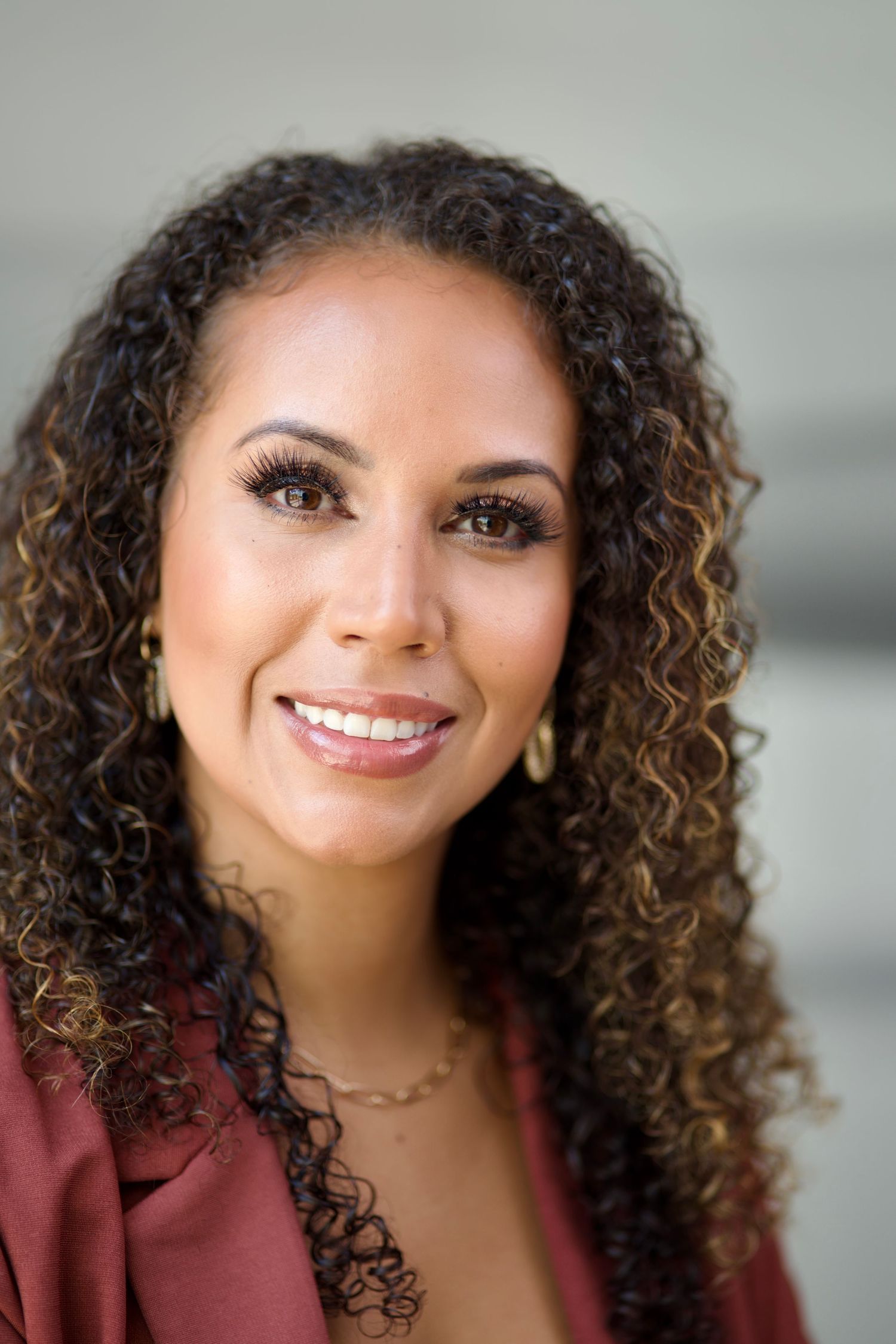 Professional headshot of woman with curly hair wearing burgundy blazer.