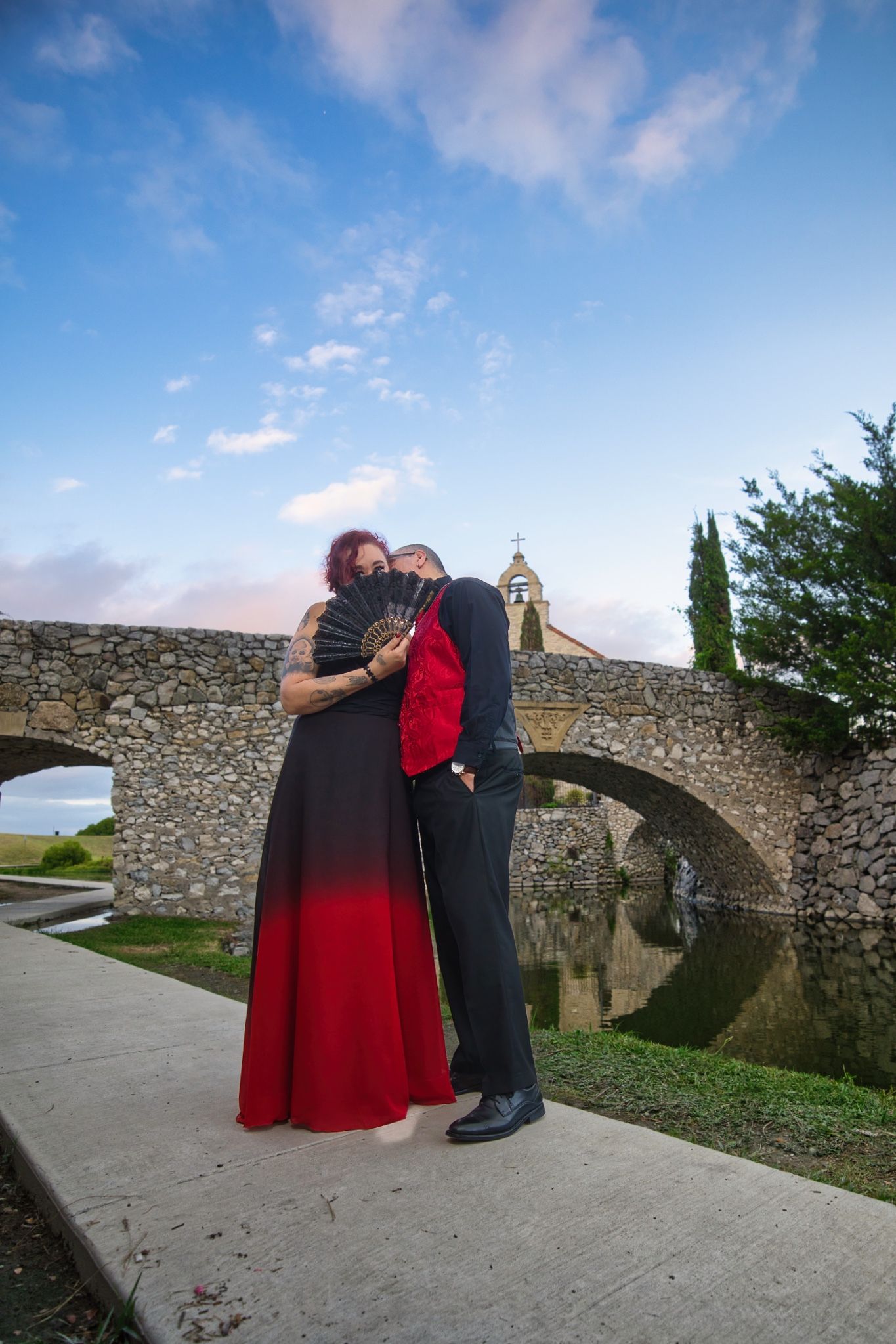 Couple embracing near stone bridge and church during sunset.