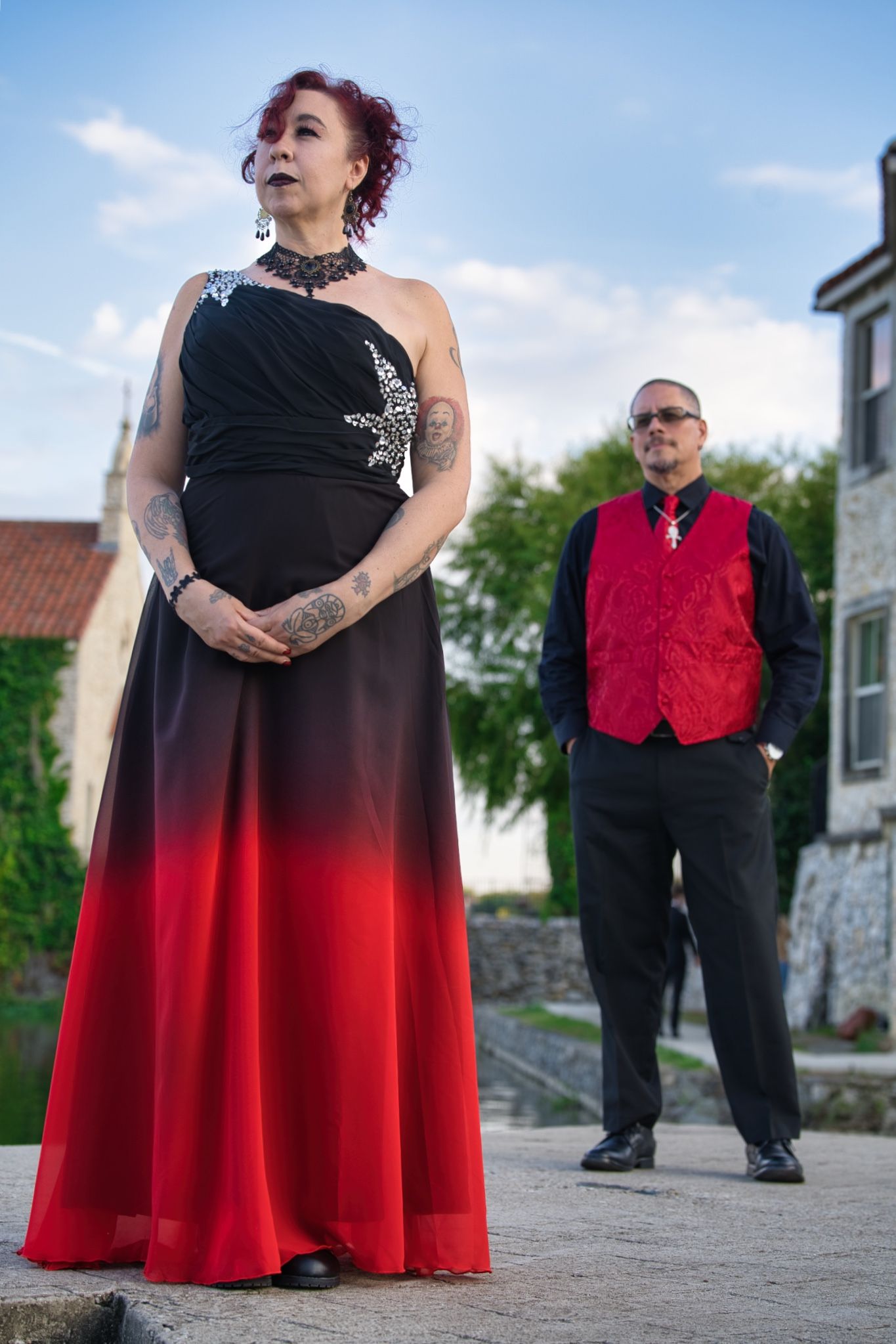 A woman in an ombre black and red dress poses in front of stone buildings.