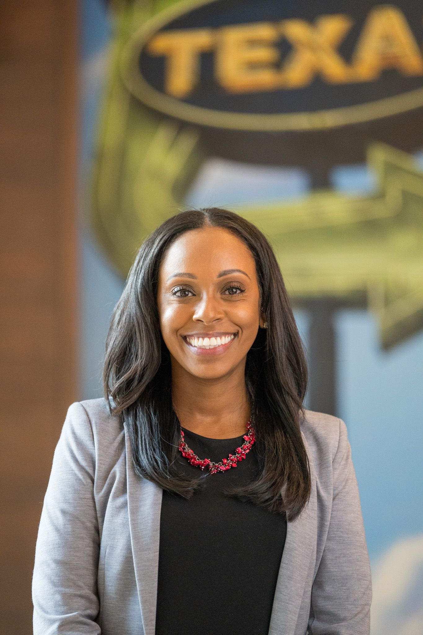 Professional woman in grey blazer and black top smiling in front of Texas sign.