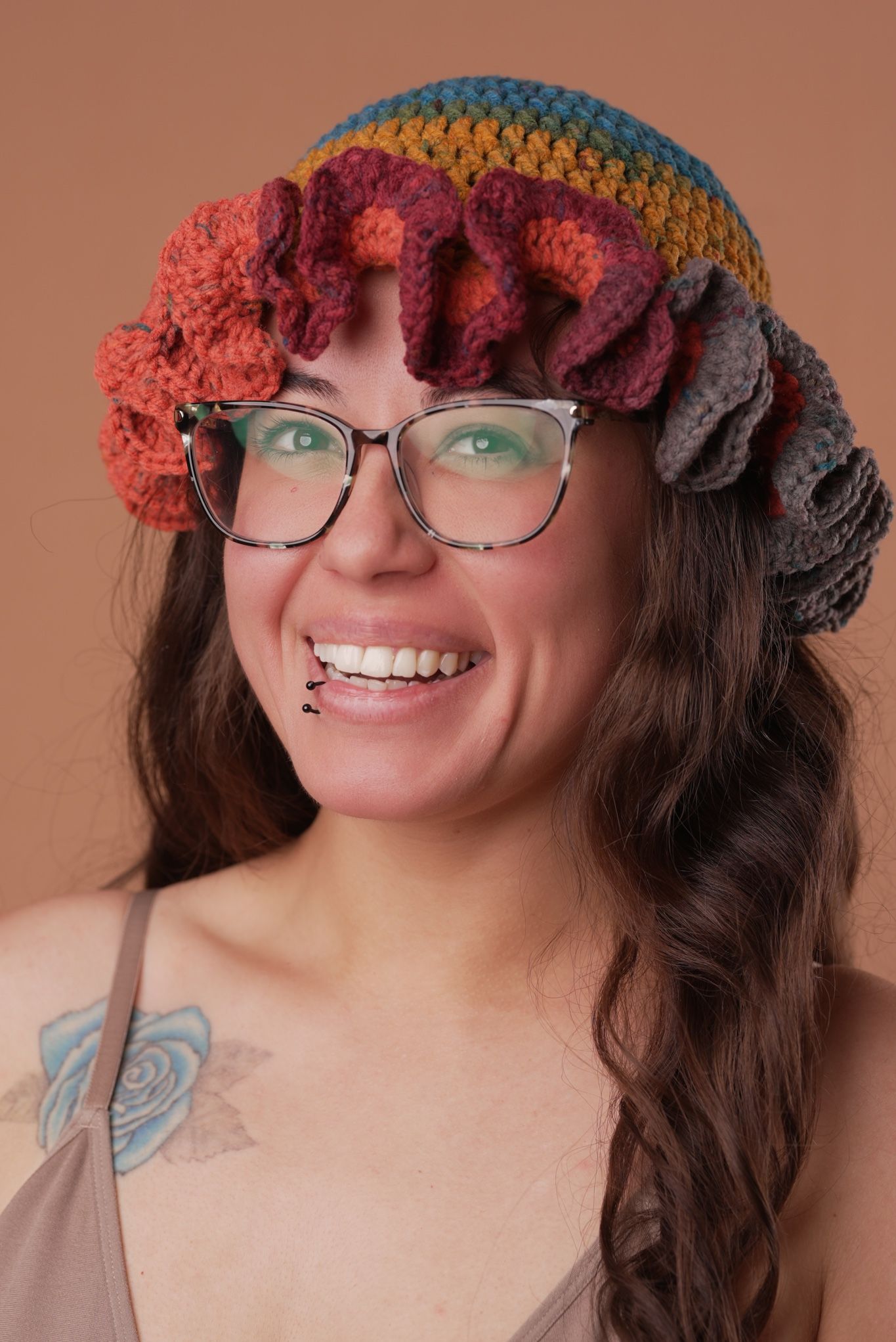 Portrait of person wearing colorful crochet beanie and glasses against brown background.