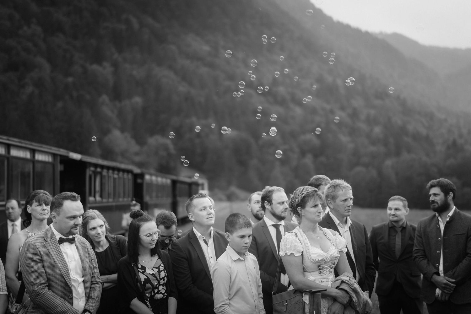 Die Gäste der Hochzeit von Jasmin und Stefan blicken ergriffen auf das Brautpaar – emotionale Szene mit Seifenblasen vor Bergkulisse.