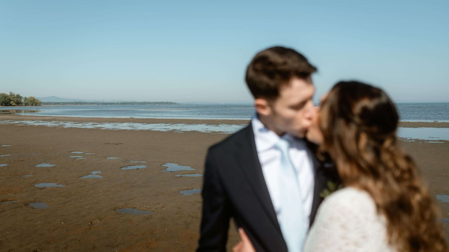 Intimer Kussmoment am Seeufer mit Blick über das Wasser – natürliche Hochzeitsfotografie von NuMa Fotografie in Vorarlberg.