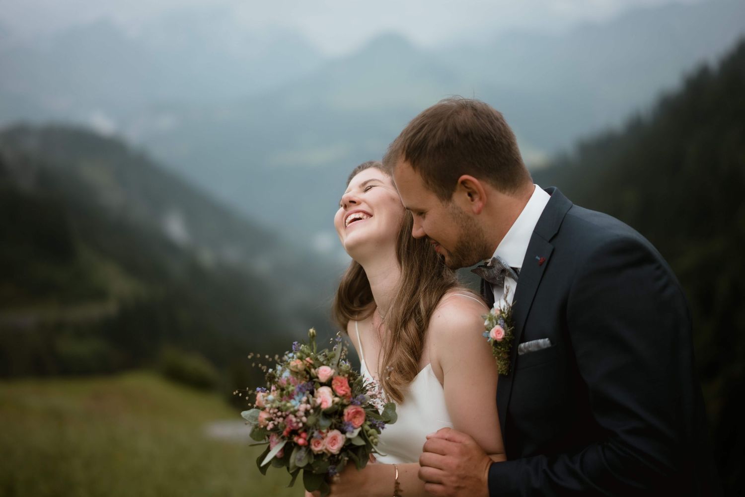 Jasmin und Stefan lachen ausgelassen inmitten der grünen Berglandschaft – lebendige Hochzeitsfotografie aus Vorarlberg.