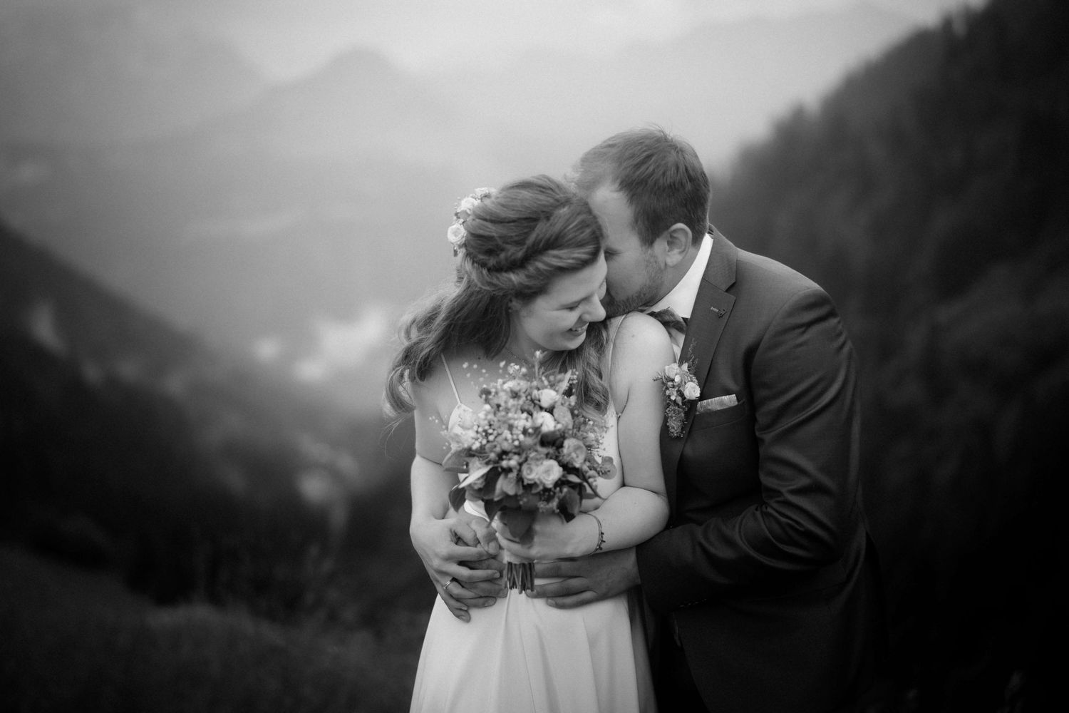 Inniger und fröhlicher Moment des Brautpaares mit Blick über die Alpen – authentische Hochzeitsbilder in Vorarlberg.