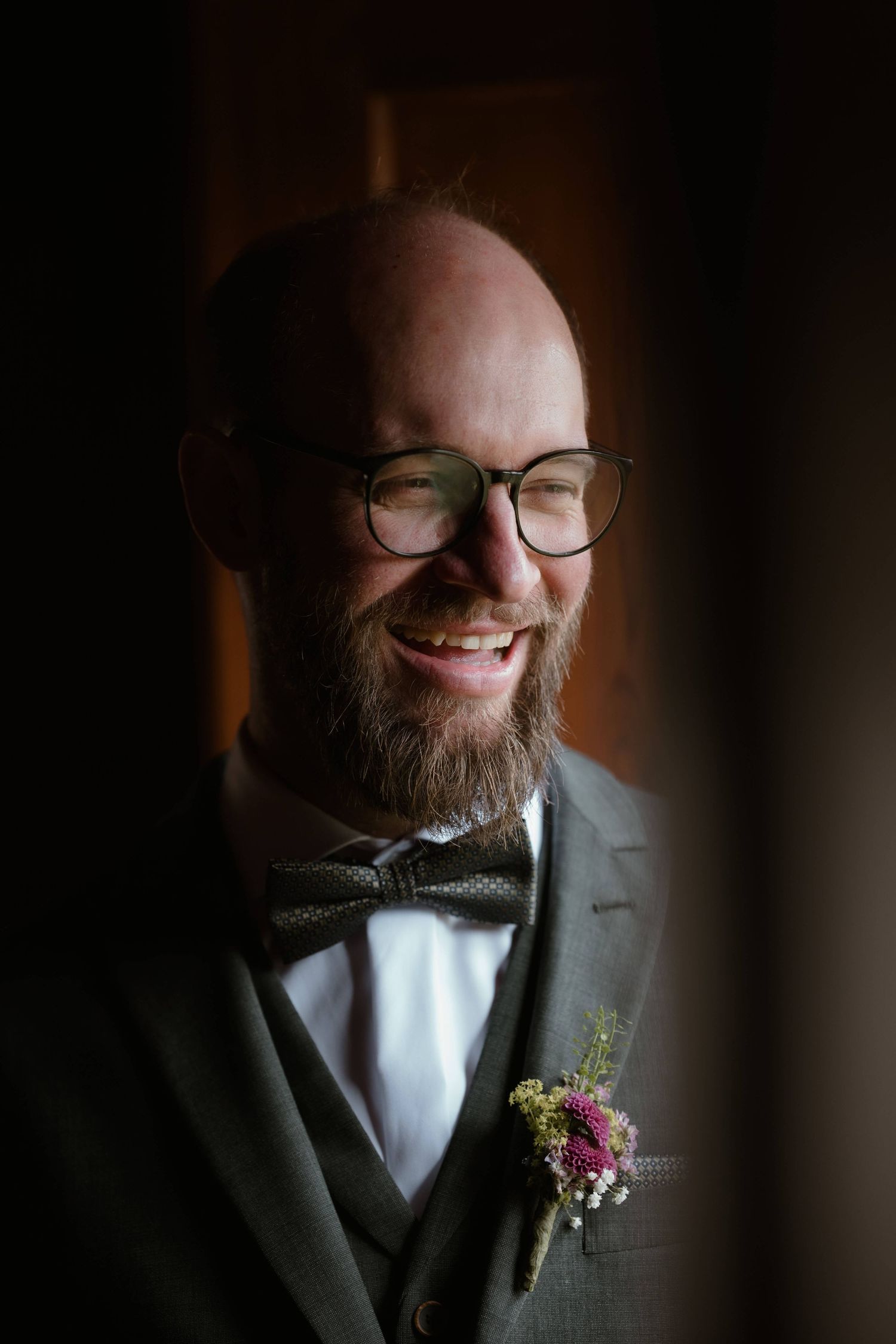 Johannes lacht herzlich in seinem eleganten Hochzeitsanzug im Tageslicht