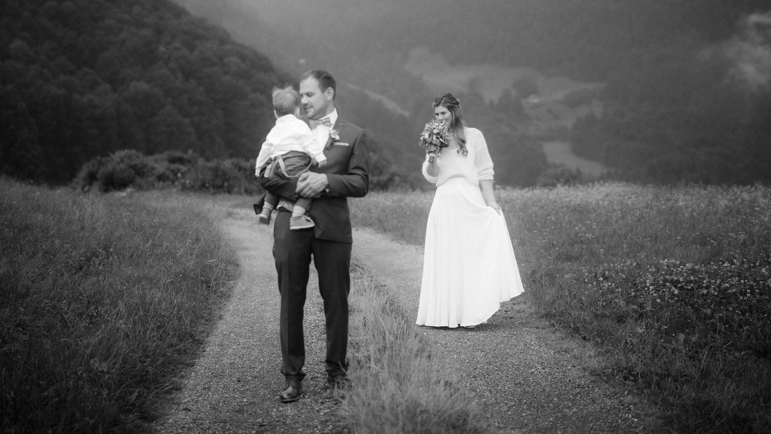 Jasmin und Stefan mit Kind auf einem Bergweg – emotionale Schwarz-Weiß-Aufnahme der Hochzeitsreportage