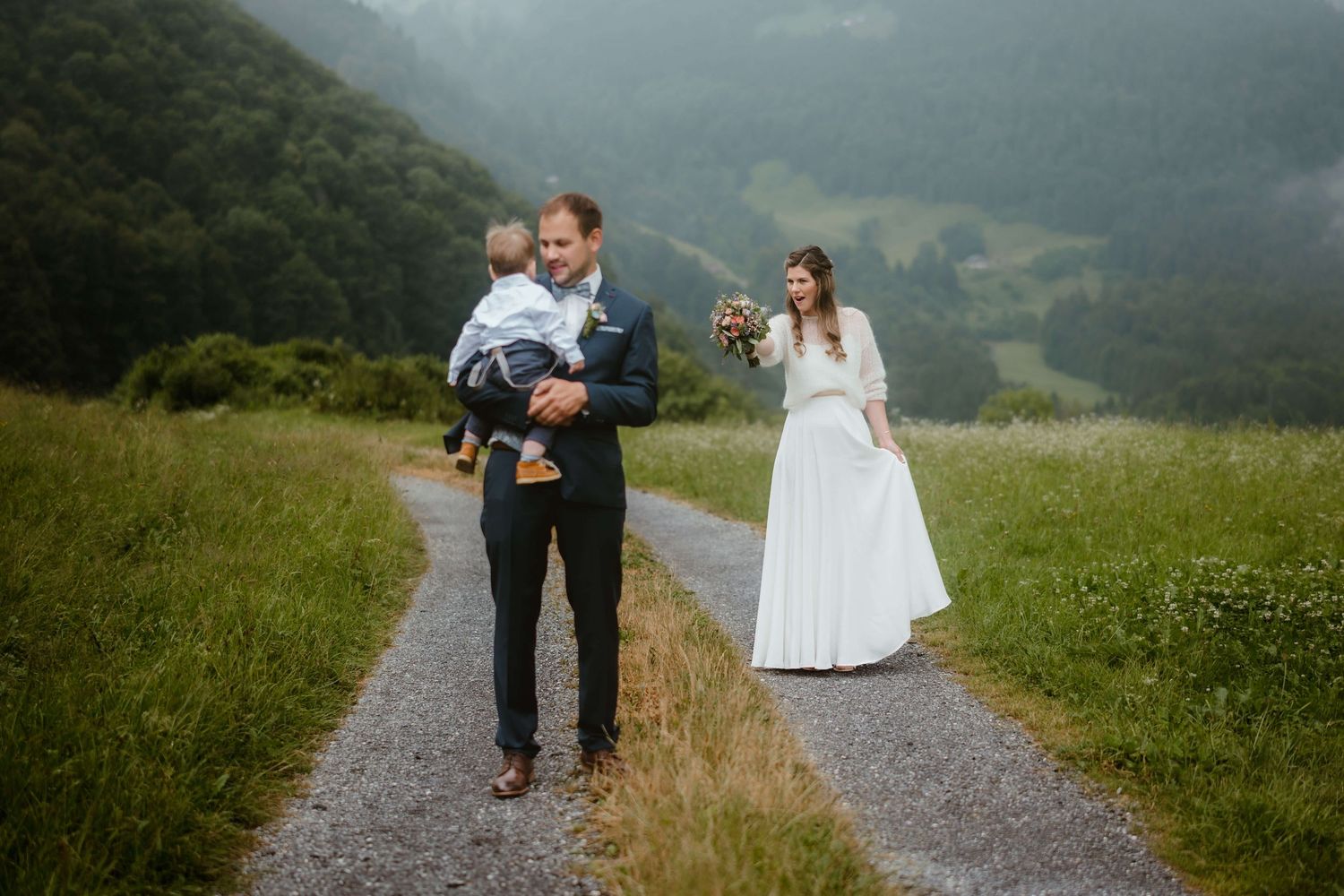 Jasmin und Stefan spazieren mit einem Kind durch die Berglandschaft – natürliche Momentaufnahme ihrer Hochzeit in Vorarlberg
