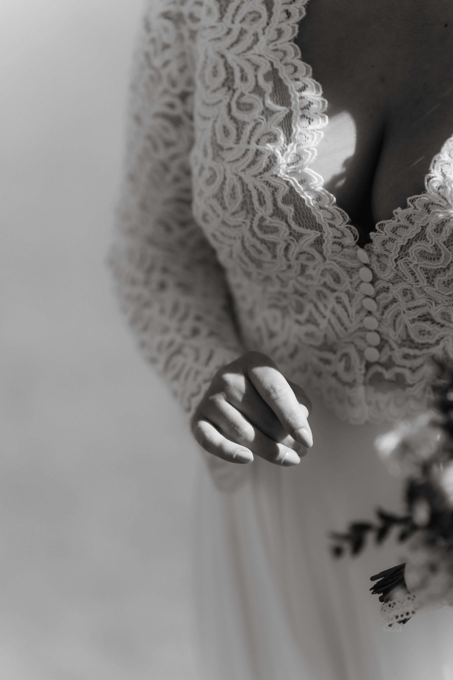 Detailaufnahme des Brautkleids in Schwarzweiß, mit Spitzenmuster und Brautstrauß – stilvolle Hochzeitsfotos von NuMa Fotografie, Bodensee.