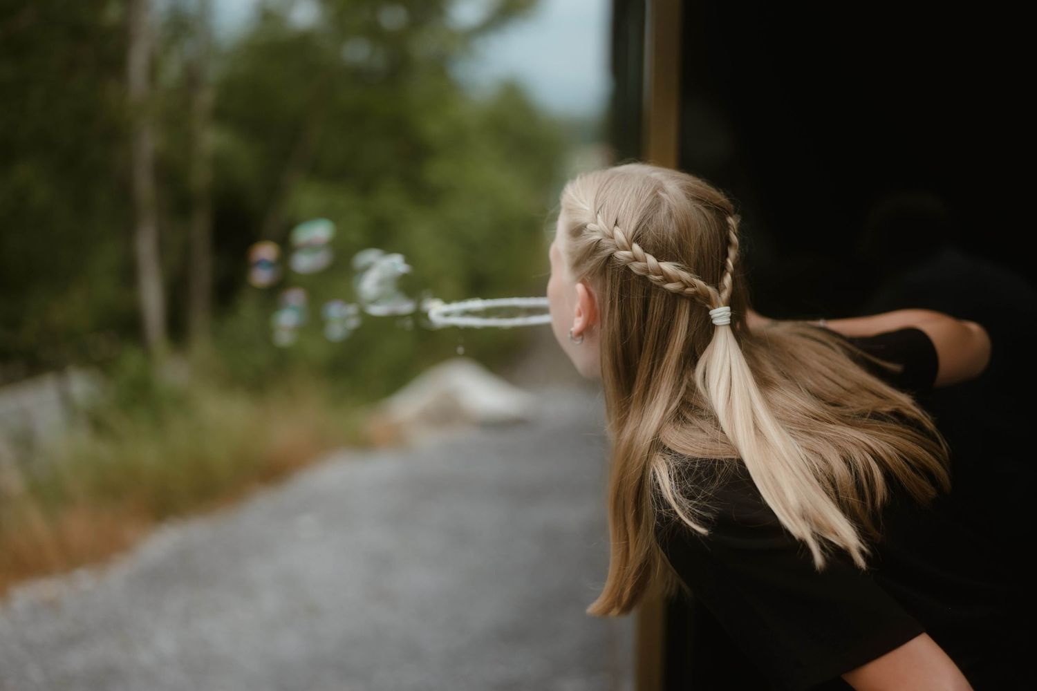 Ein blondes Mädchen mit geflochtenen Zöpfen pustet spielerisch Seifenblasen bei einer Hochzeit in Vorarlberg – eingefangen von NuMa Fotograf