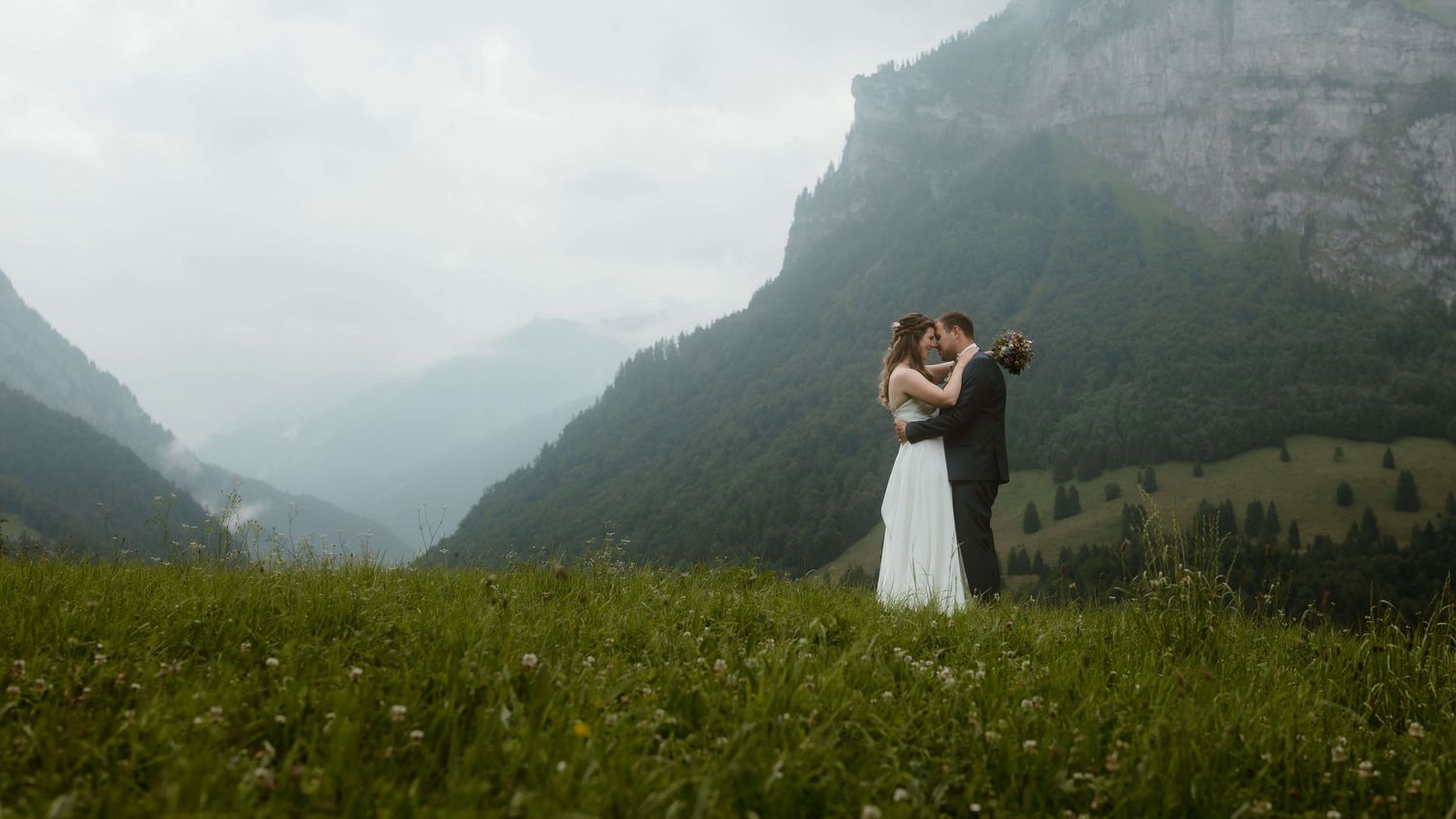 asmin und Stefan umarmen sich auf einer Bergwiese in Vorarlberg – ein emotionaler Augenblick mit Alpenpanorama im Hintergrund